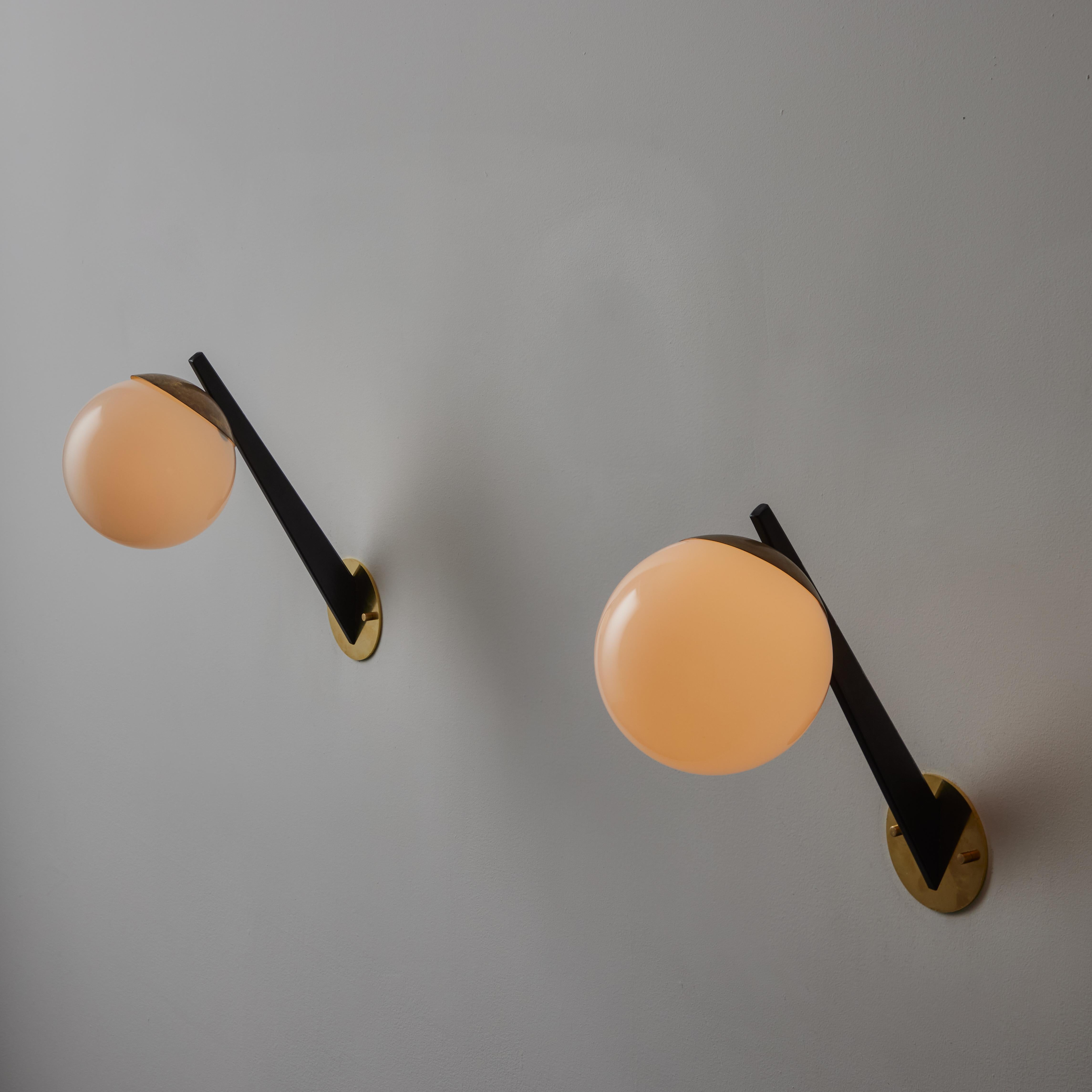 Pair of Sconces by Stilnovo. Designed and manufactured in Italy, circa the 1950s. Angular black enameled armatures paired with white opaline glass diffusers. Each sconce holds and e14 socket type adopted for the US. We recommend a 40 W or LED