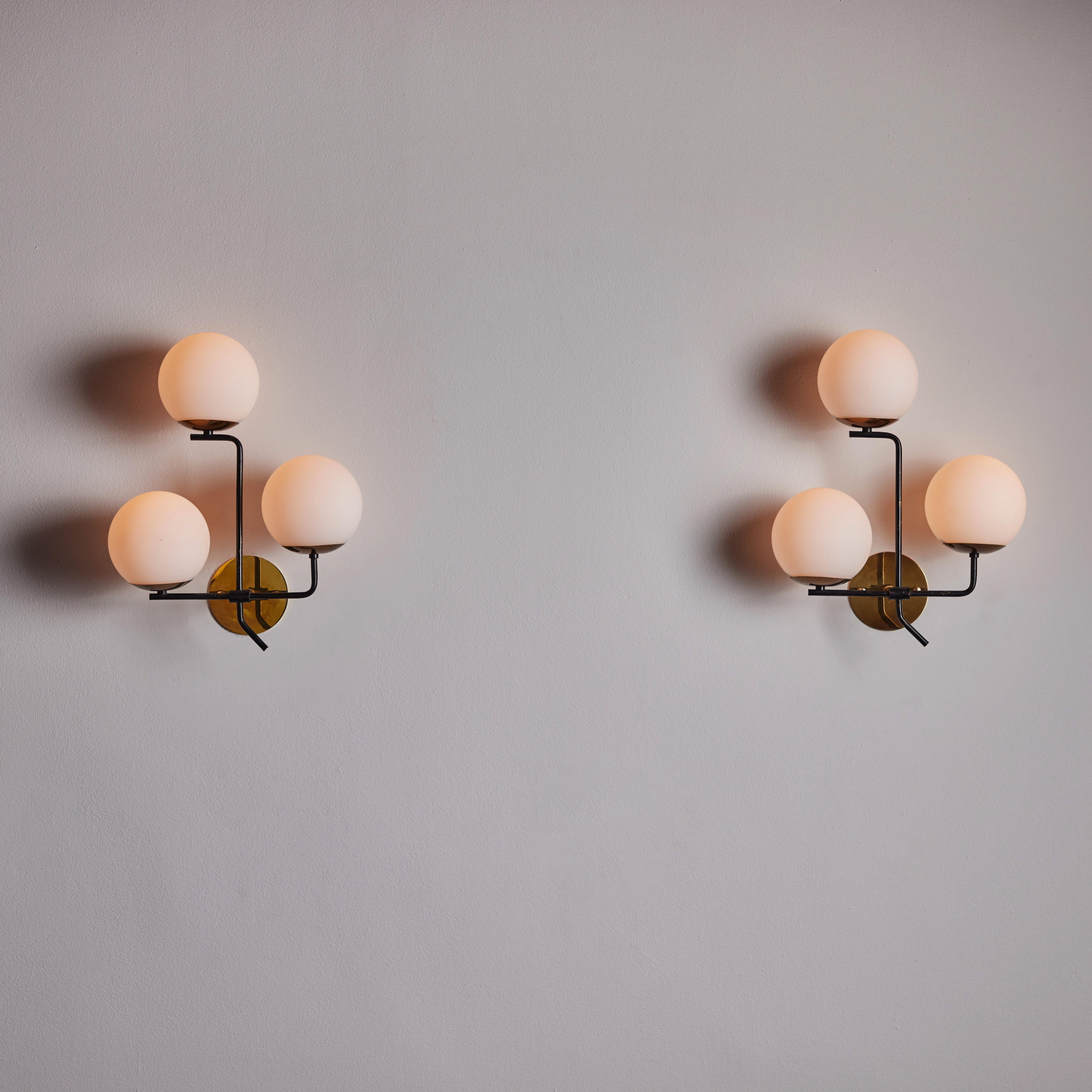 Pair of sconces by Stilnovo. Designed and manufactured in Italy, circa the 1950s. Three-arm stems, each cradling a frosted glass globe. Rewired for U.S. standards. We recommend three E14 20W Max bulbs per fixture. Bulbs are included as a one-time