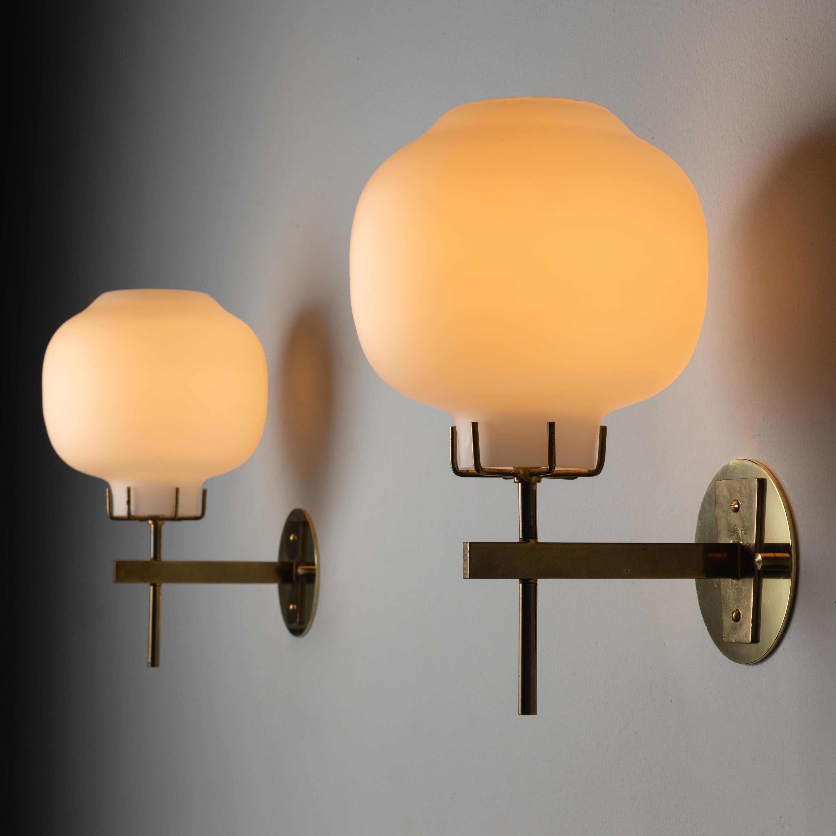 Pair of Sconces by Stilnovo. Designed and manufactured in Italy, circa the 1960s. An opal glass orb is nested onto a brass fixture stem. Brass has been aged throughout. Custom backplate for US applications. Wired for US standards. Each sconce takes
