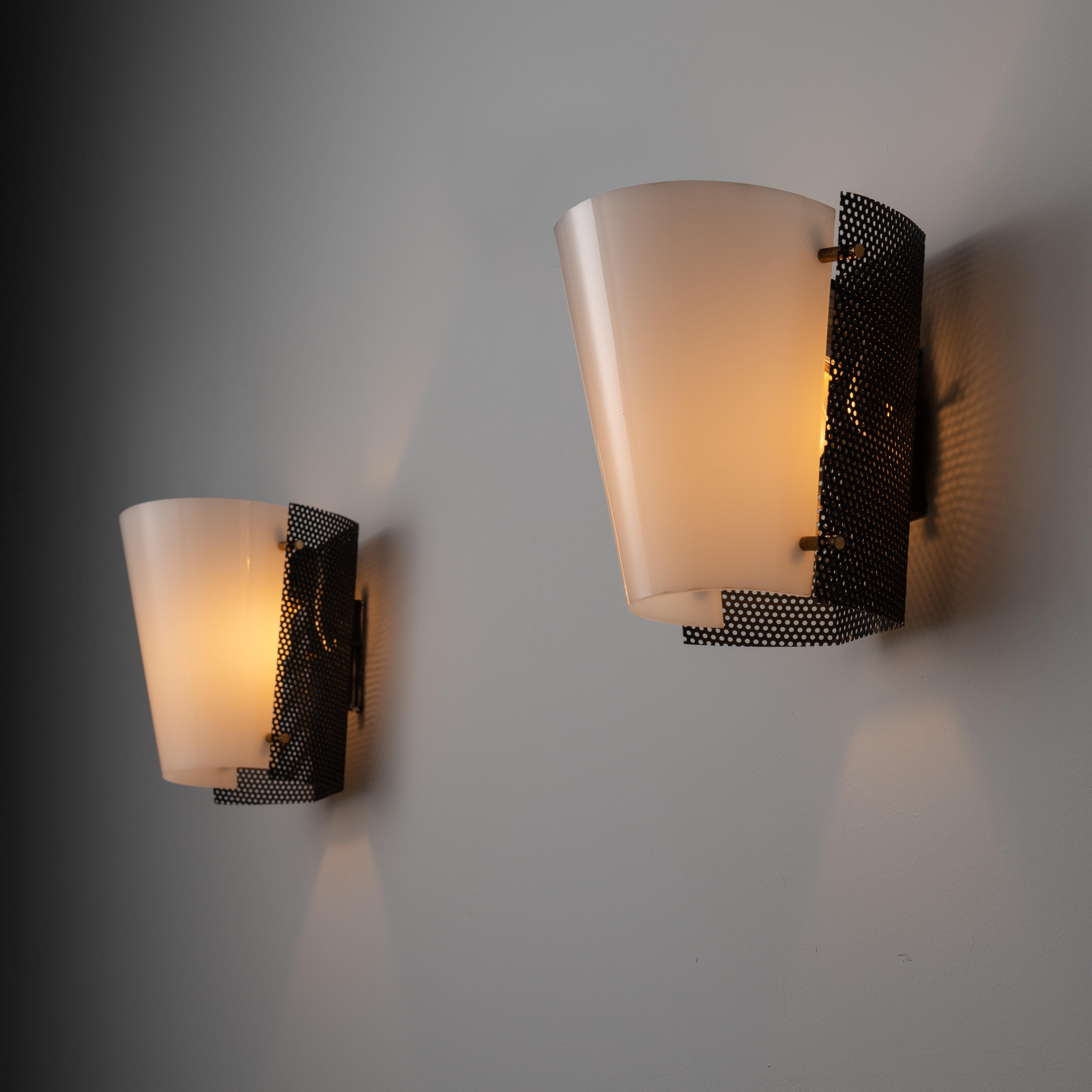 Pair of sconces by Stilnovo. Designed and manufactured in Italy, in 1955. Wall sconces with soft white acrylic diffusers, perforated black formed side paneling and brass hardware detailing. Each sconce holds one E27 bulb socket, adapted for the US.