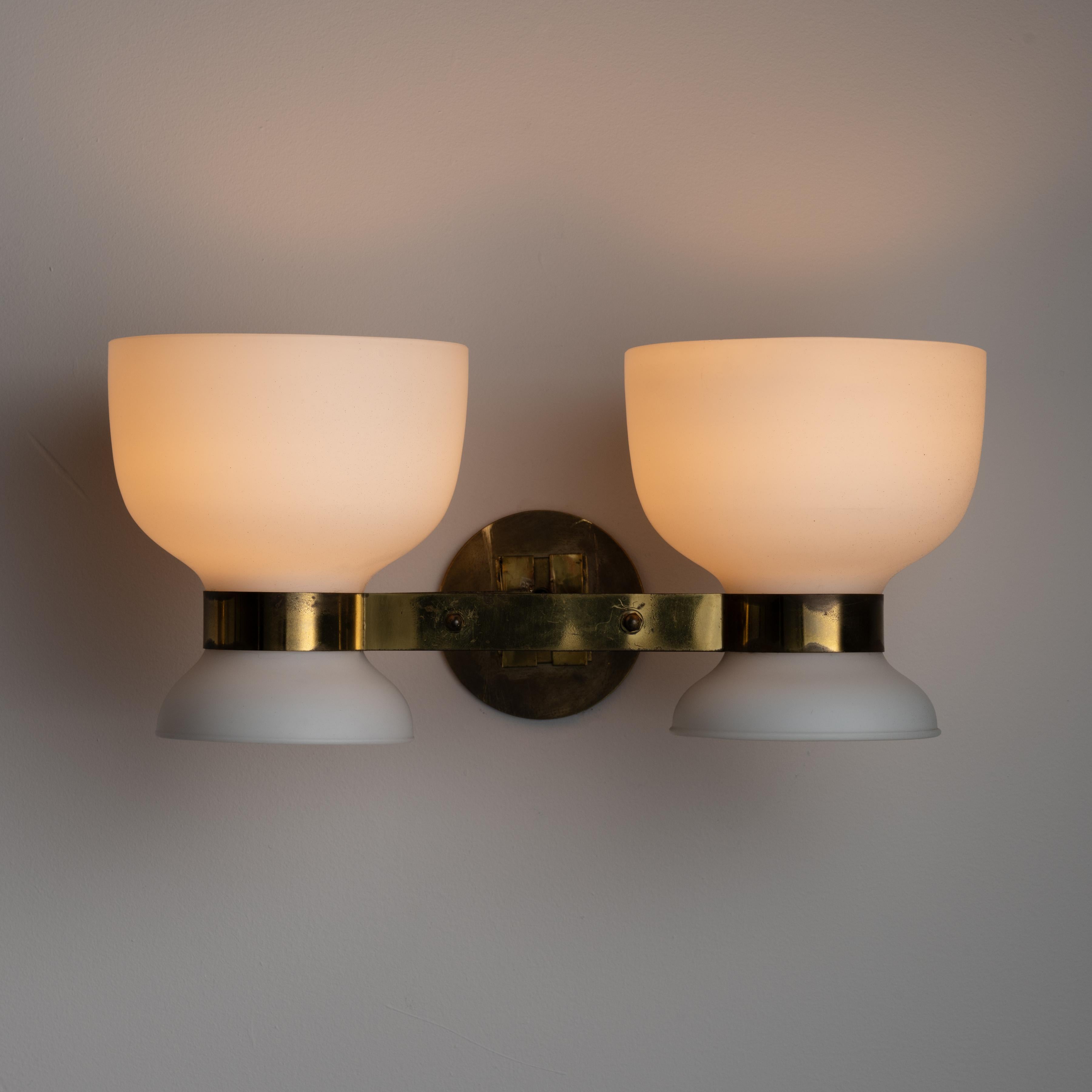 A pair of sconces by Stilnovo. Designed and manufactured in Italy, circa the 1950s. Dual opal white chalices with aged brass holders. Custom US backplate. Wired for the US. Sold as a pair.