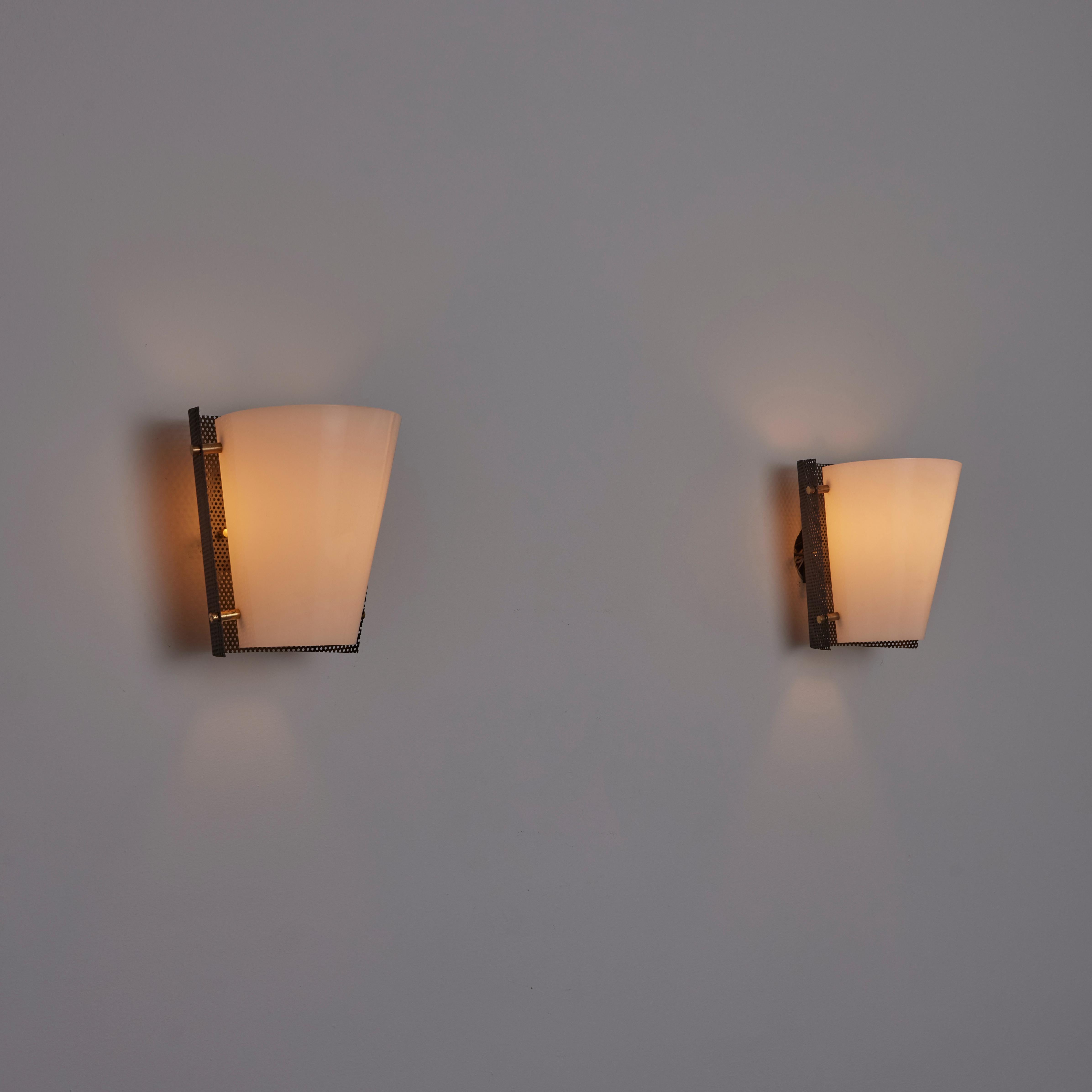 Pair of sconces by Stilnovo. Designed and manufactured in Italy, in 1955. Wall sconces with soft white acrylic diffusers, perforated black formed side paneling and brass hardware detailing. Each sconce holds one E27 bulb socket, adapted for the US.