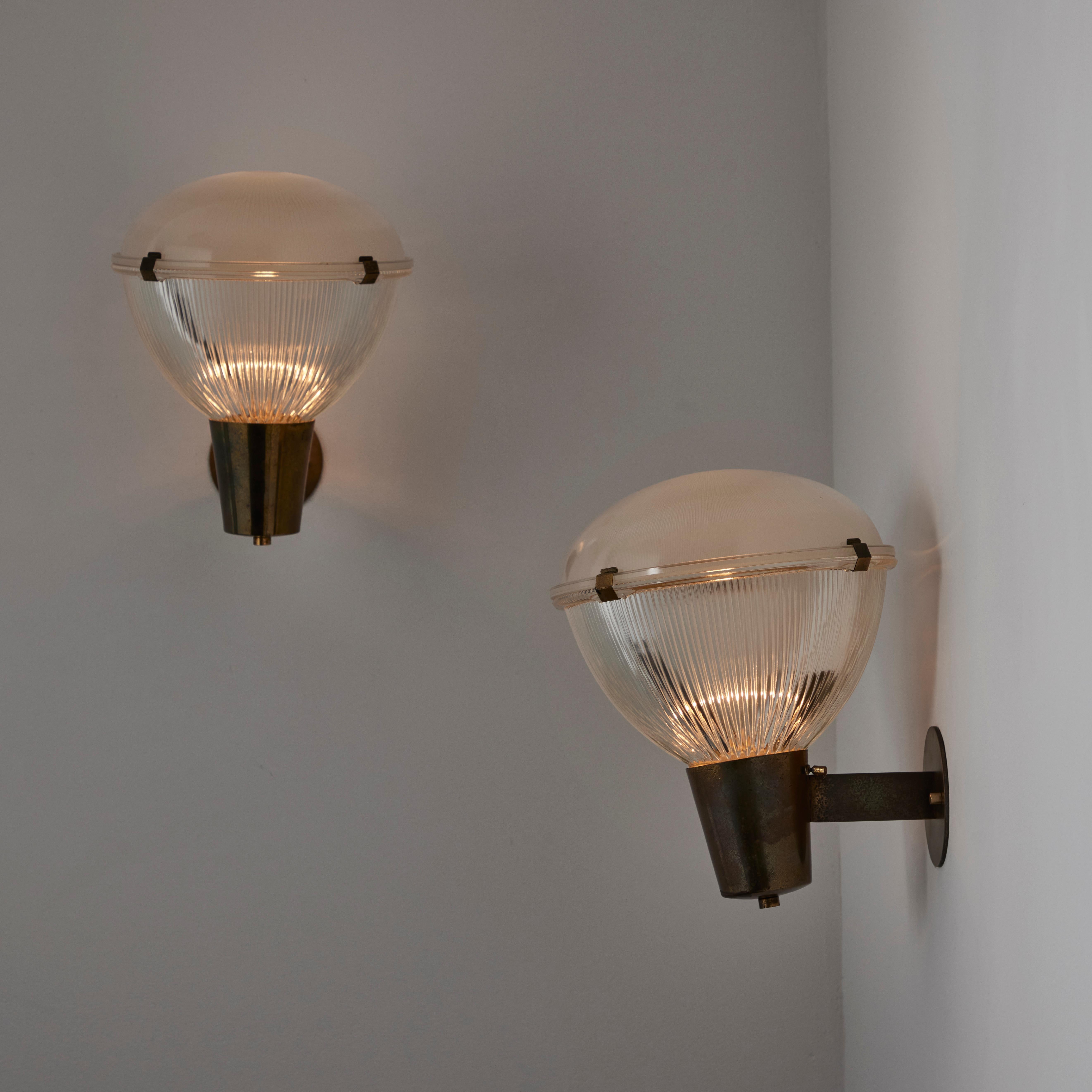 Pair of Sconces by Stilnovo. Designed and manufactured in Italy, circa the 1960s. Reeded glass bottom and top glass diffusers are clipped together and paired with aged polished patinated brass. Each light holds a single E14 socket type, adapted for