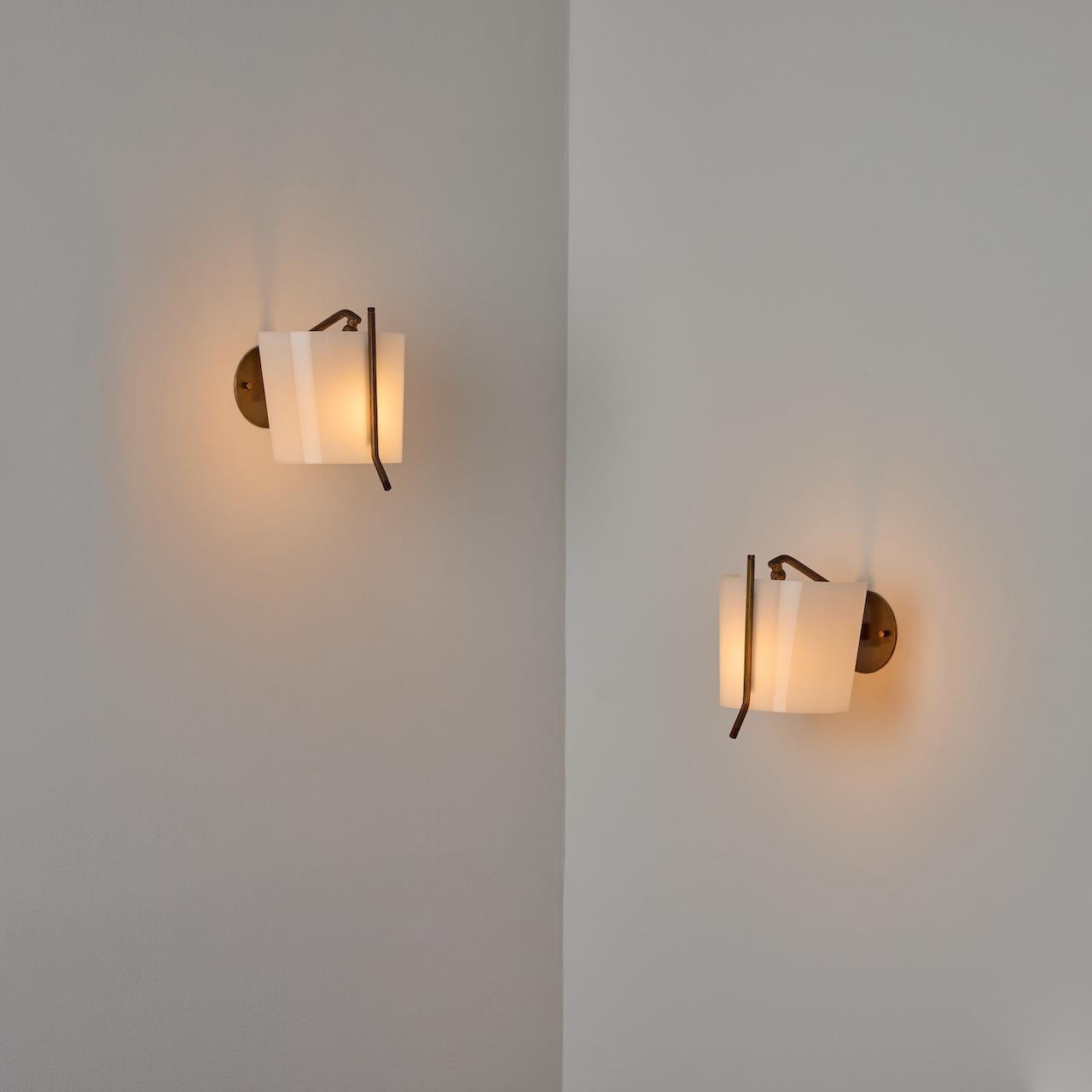 Pair of Sconces by Stilnovo. Designed and manufactured in Italy, circa the 1960s. Lucite bent shields with beautifully aged brass details. Articulation vertically and outwardly on the shield are possible. Each sconce holds a single E14 socket type,