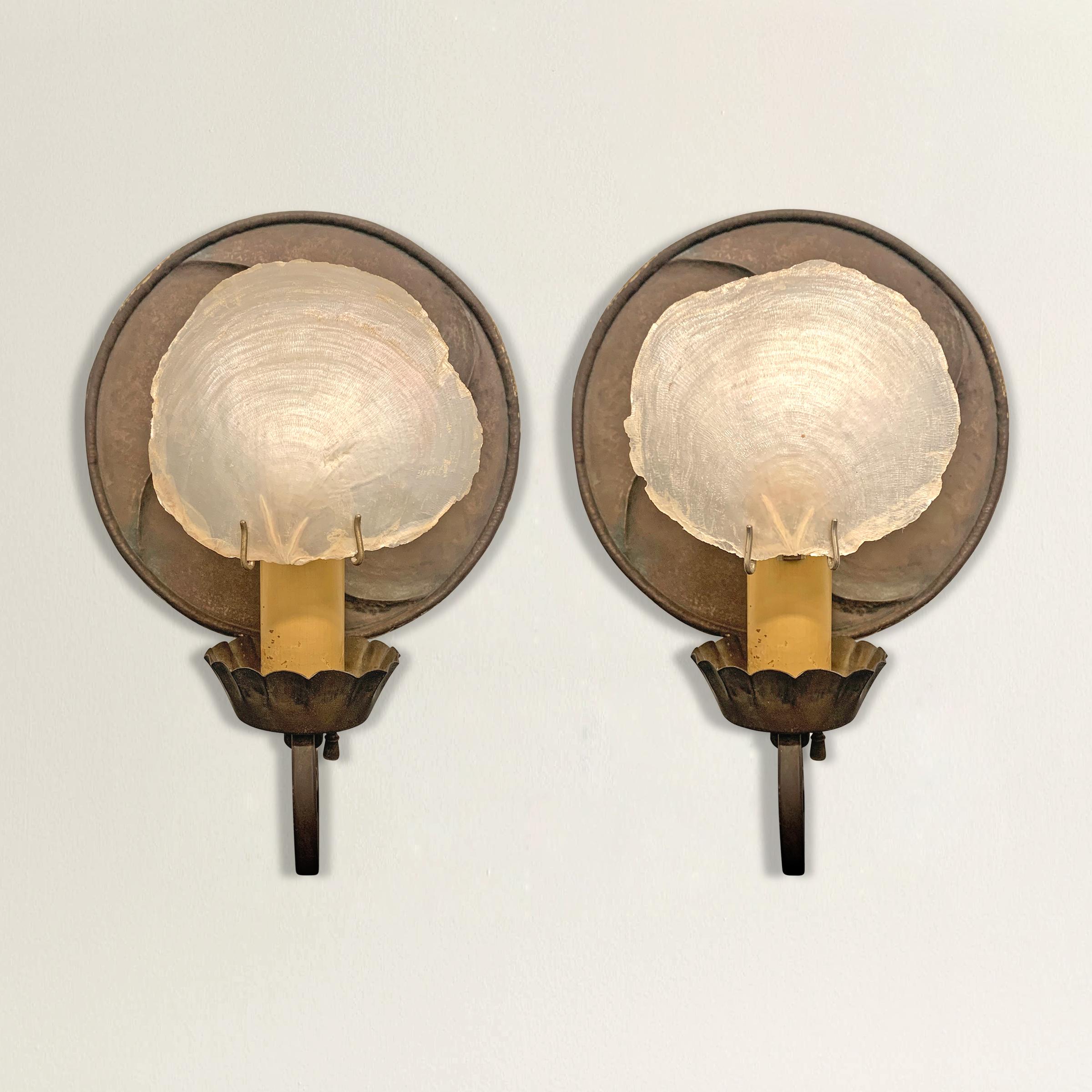 A pair of incredible sconces designed by east coast architect, Frank Forster, each with a hand-hammered circular steel backplate, a single arm with a scalloped candle cup, and a capiz shell shade. The capiz shell shades are probably not original,