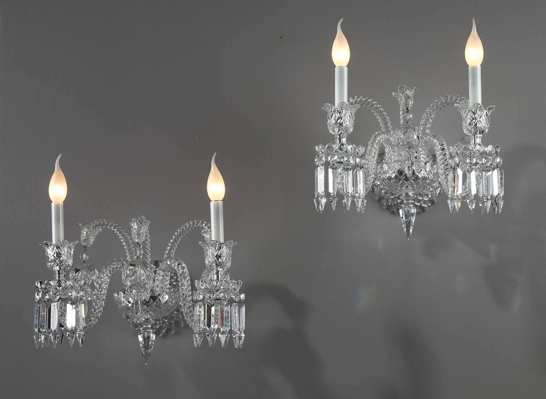 Pair of Baccarat crystal sconces with two arms of lights. Each sconce is decorated with geometric pendants. Each one has three purely decorative arms decorated with a large crystal flower pendant. The shafts are twisted. The sconces are signed
