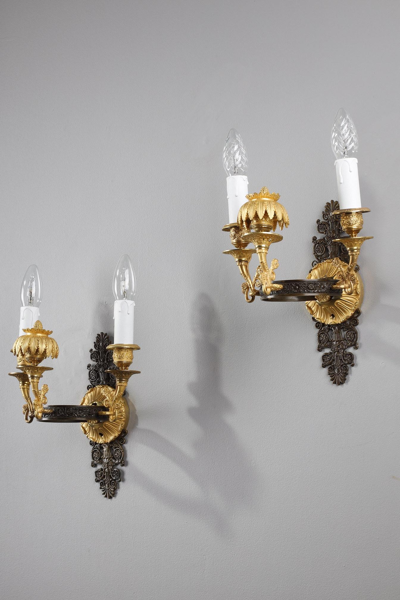 Pair of ormolu sconces, patinated and chiseled, from the Charles X period. Two arms of light are arranged on either side of a central branch decorated with leaves coming out of the binet and topped by a pine cone. These three branches are attached