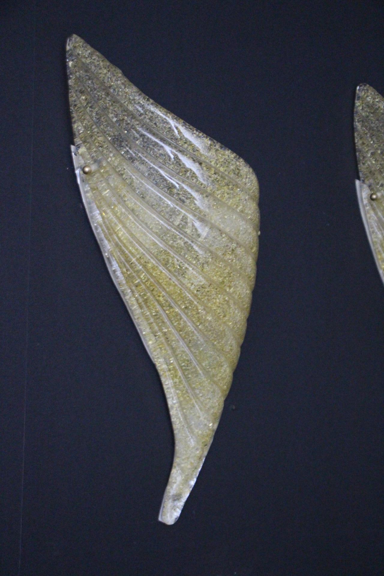 This pair of Murano glass sconces is very poetic because their design could suggest wings shapes.Its hand blown glass with textured ribbed horizontal patterns and granular effect using Graniglia technique and golden flakes inclusions provides a very