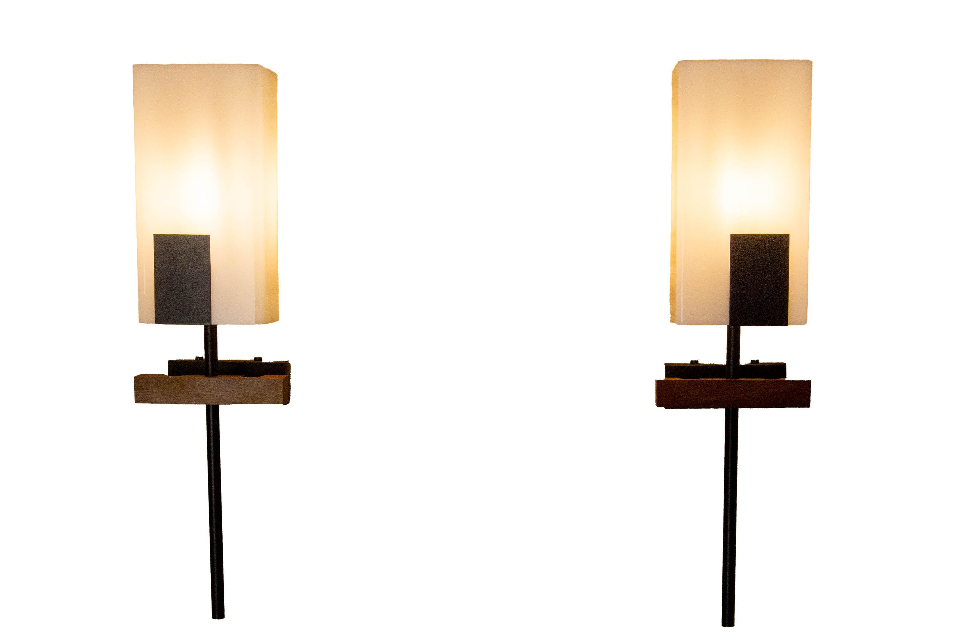 Pair of wall lights with a geometric design typical of the 1960s, combining a black metal structure, a wooden base, and a rectangular opal glass diffuser. 
The clean lines and contrasting materials reflect the influence of the modernist design of