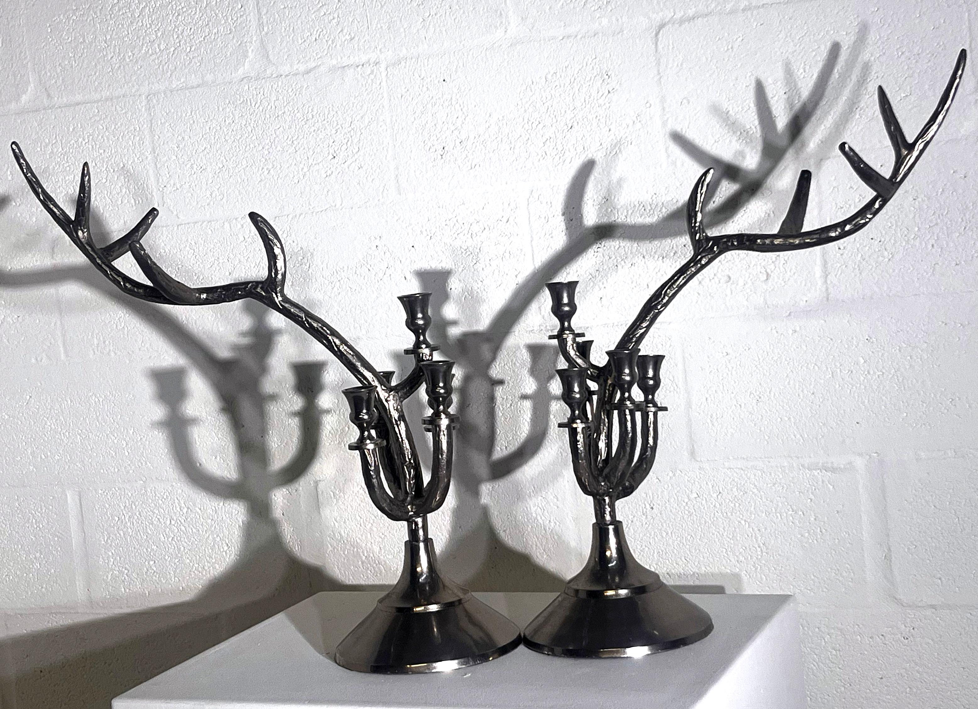 A striking pair of sculptural candelabra crafted in polished metal, designed in the form of branching deer antlers. Each piece combines a traditional candelabrum base with five candle holders that extend upward into elongated, naturalistic antler