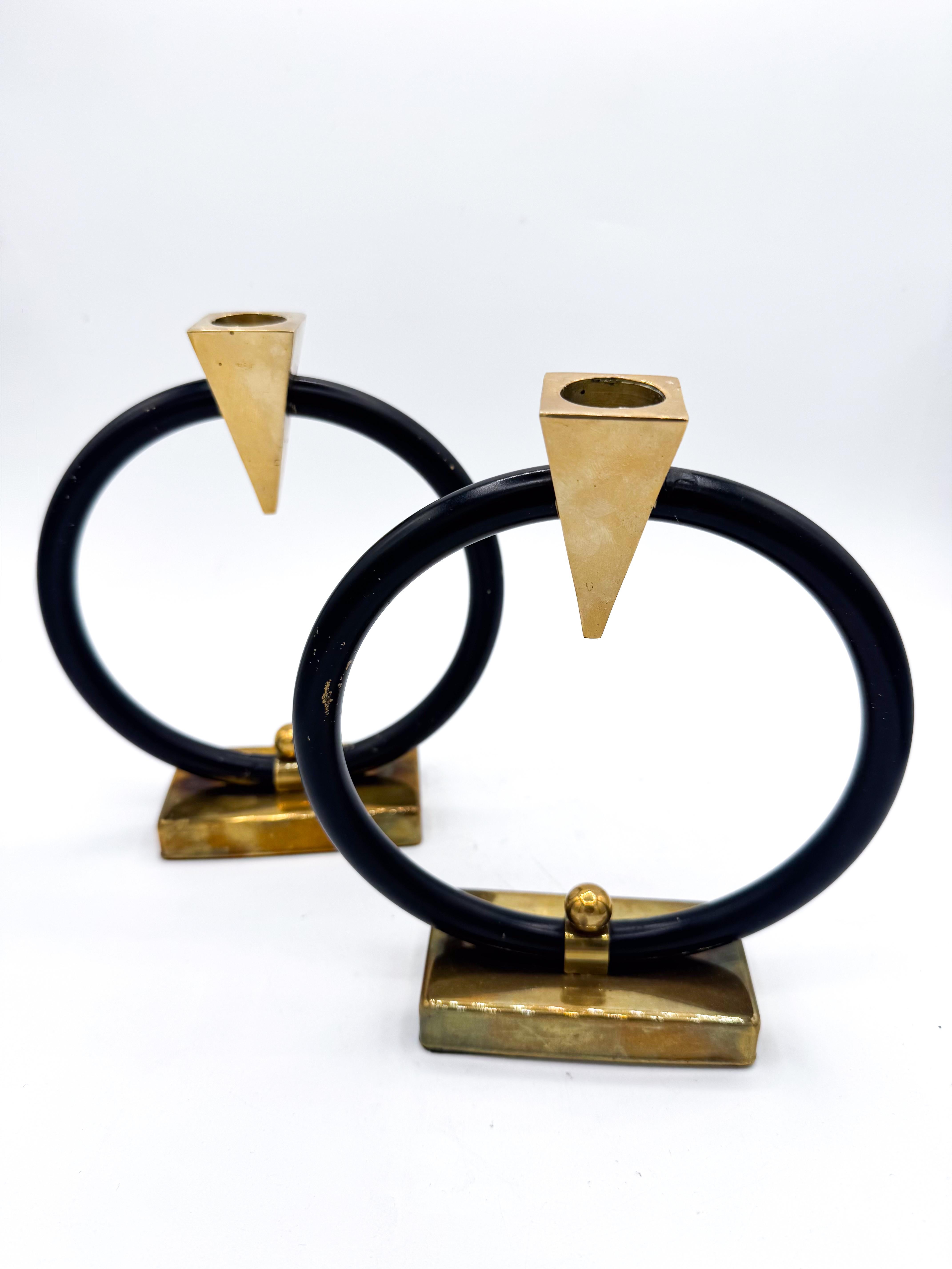 Questa coppia di portacandele postmoderni è un esempio della raffinatezza scultorea del design europeo degli anni Ottanta. Ogni pezzo è caratterizzato da un audace anello circolare nero in equilibrio su una sostanziosa base in ottone e coronato da