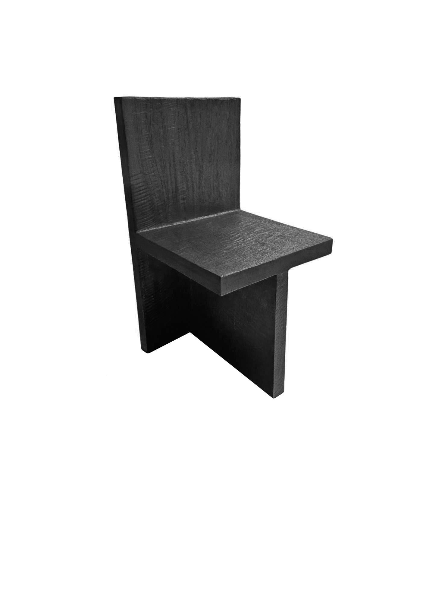 Este par de sillas de madera de mango presentan un llamativo diseño escultural, definido totalmente por líneas rectas y contornos geométricos. Las sillas, fabricadas con madera de mango de origen sostenible, están acabadas en un intenso tono negro