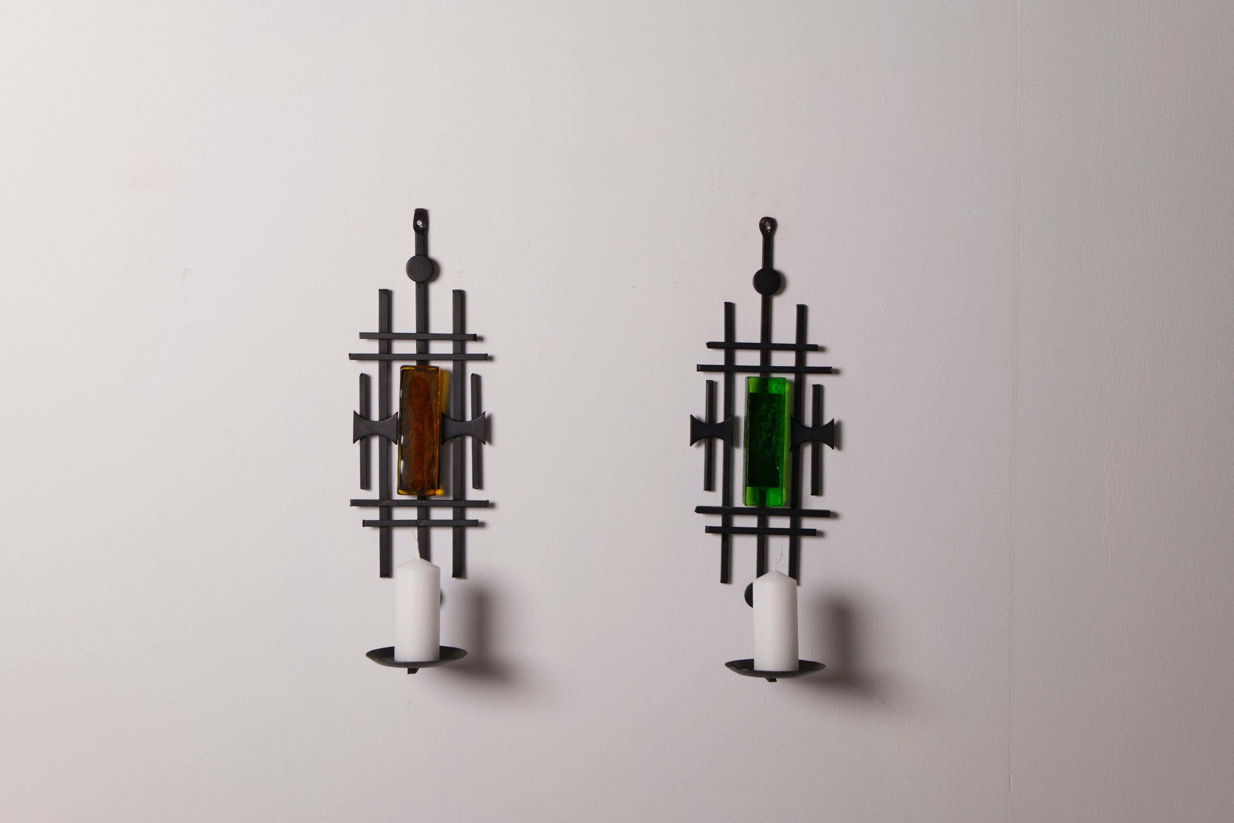 Striking pair of Danish wall-mounted candle sconces produced by Dantoft Kunstartikler in the 1970s. Each sconce is crafted from hand-forged steel with an expressive, sculptural form and features inset colored glass elements that catch and reflect