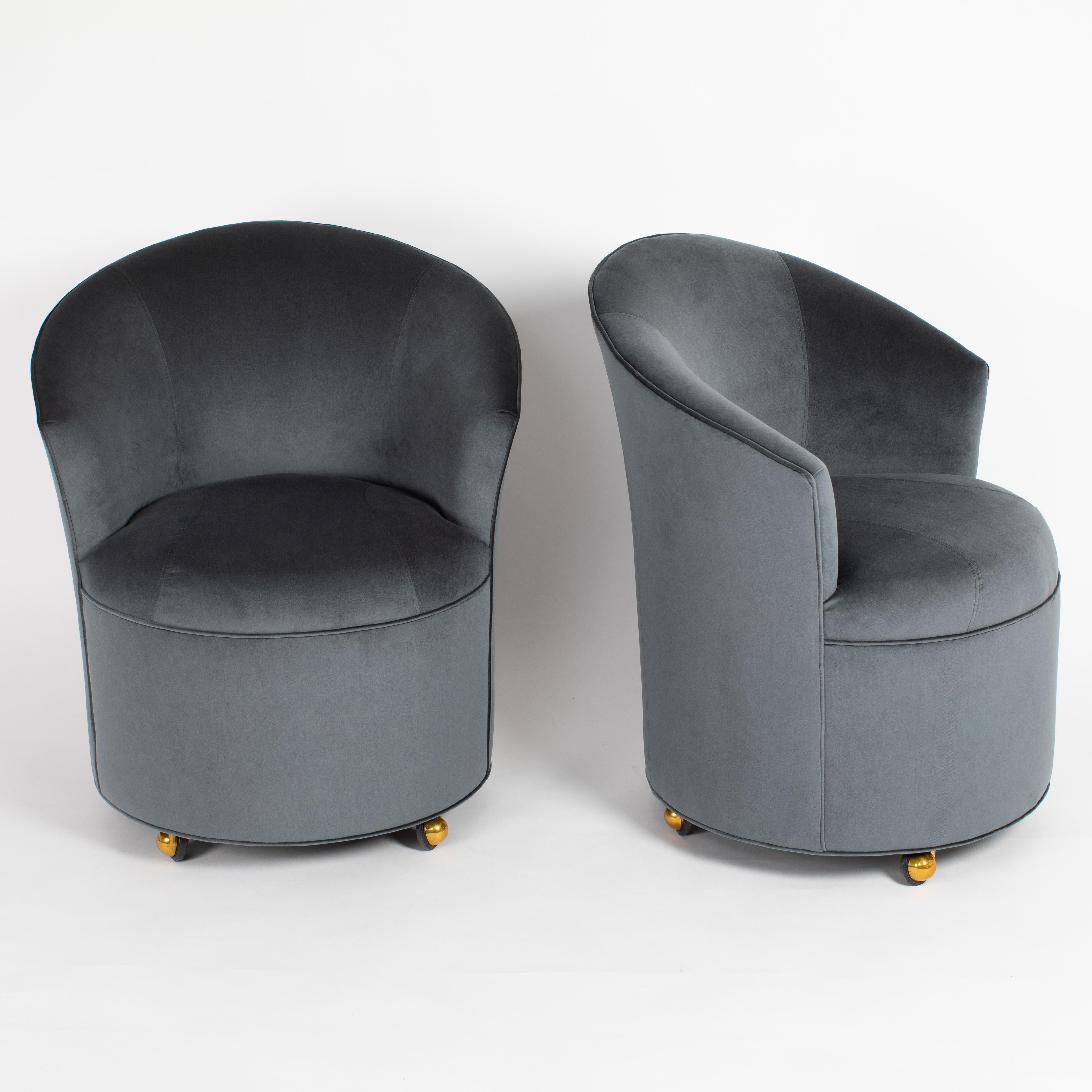 These crisp and tailored barrel chairs on brass casters feature sloping backs and integrated arms over fixed seats and fully upholstered bases. Newly upholstered in a blue-green velvet. These chairs have very elegant lines they are by directional