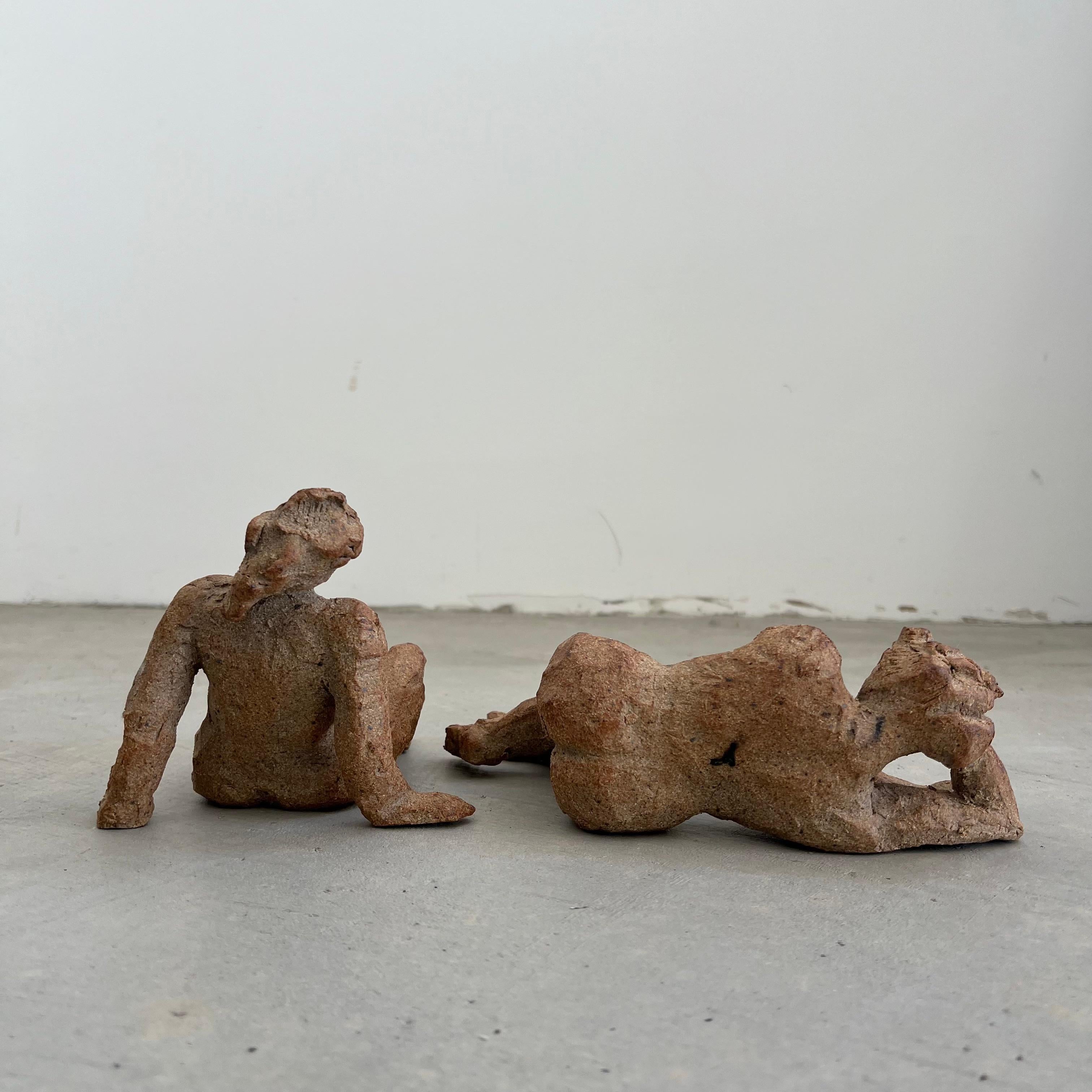 Questa suggestiva coppia di figure scultoree cattura la tranquilla intimità del riposo e della riflessione. Realizzate in gres strutturato, le due donne sono ritratte in forme organiche che bilanciano forza e vulnerabilità. Le loro posture, una