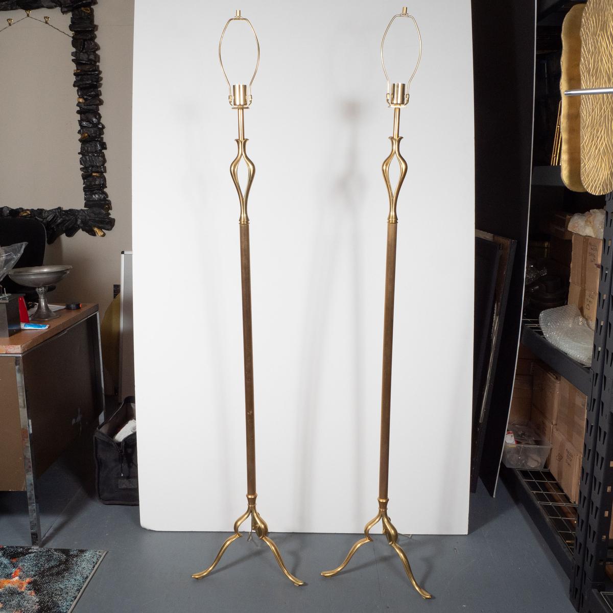 Pair of fluted brass floor lamps with sculptural details and tripod curvilinear bases.