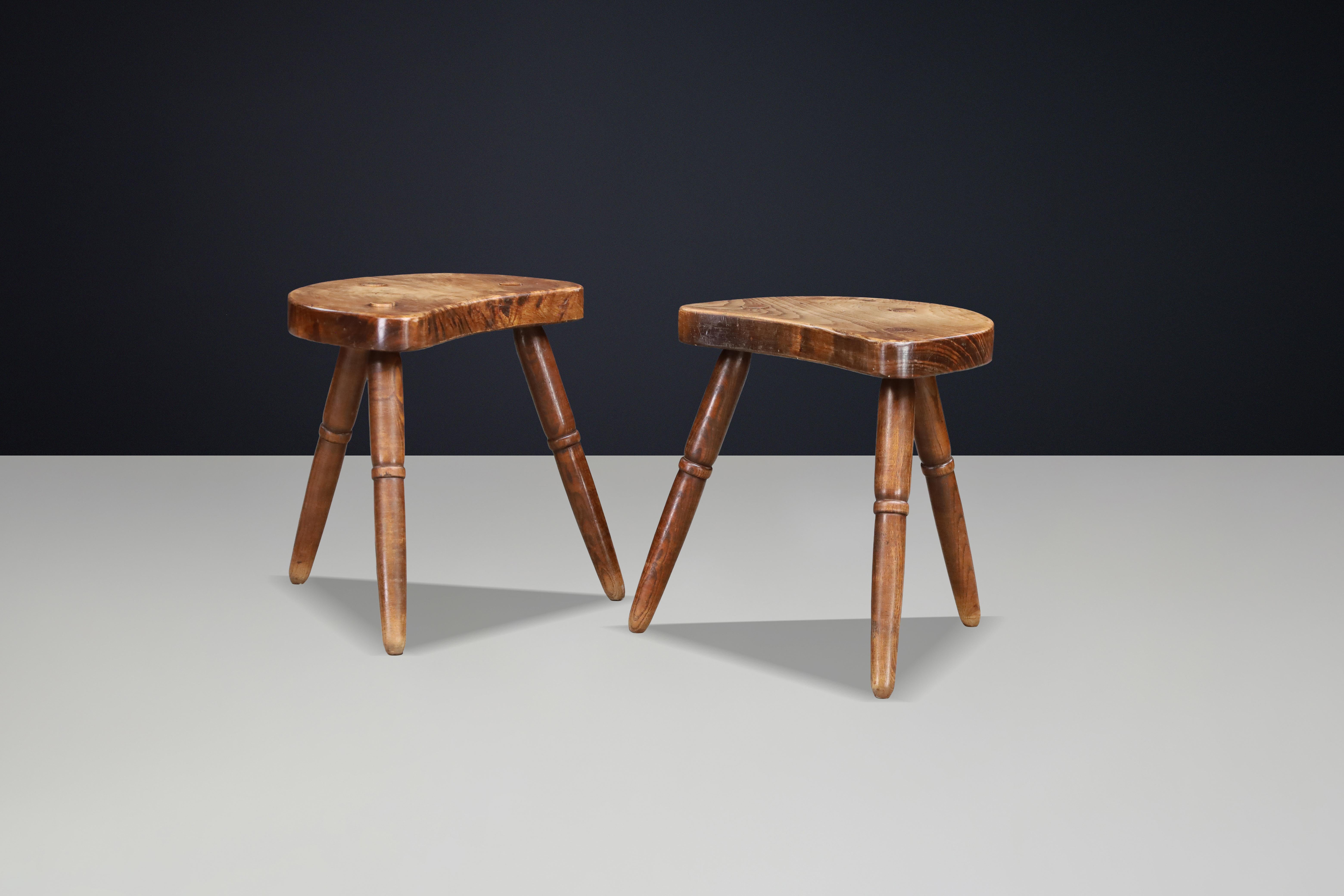 A sculptural pair of French rustic stools crafted in solid walnut, France, circa 1940s.

Each stool features a thick, organically carved saddle seat, shaped from solid walnut and showcasing expressive natural grain patterns. The seats are supported
