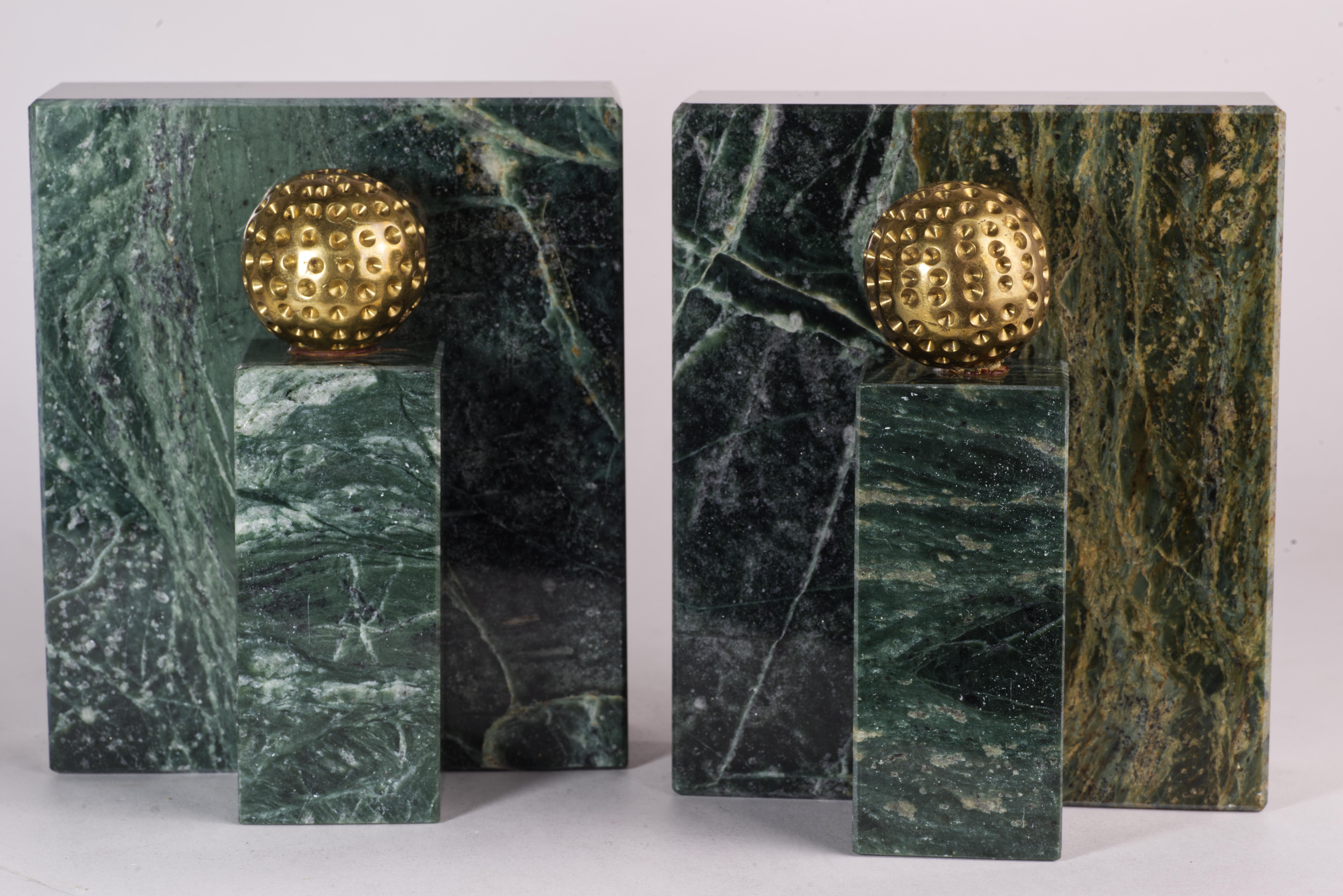  Heavy, sculptural marble bookends are decorated with brass golf balls accents. Colorful, polished, richly veined green marble contrasts with textured brass accents, creating a strong presence and adding visual interest to otherwise minimally shaped