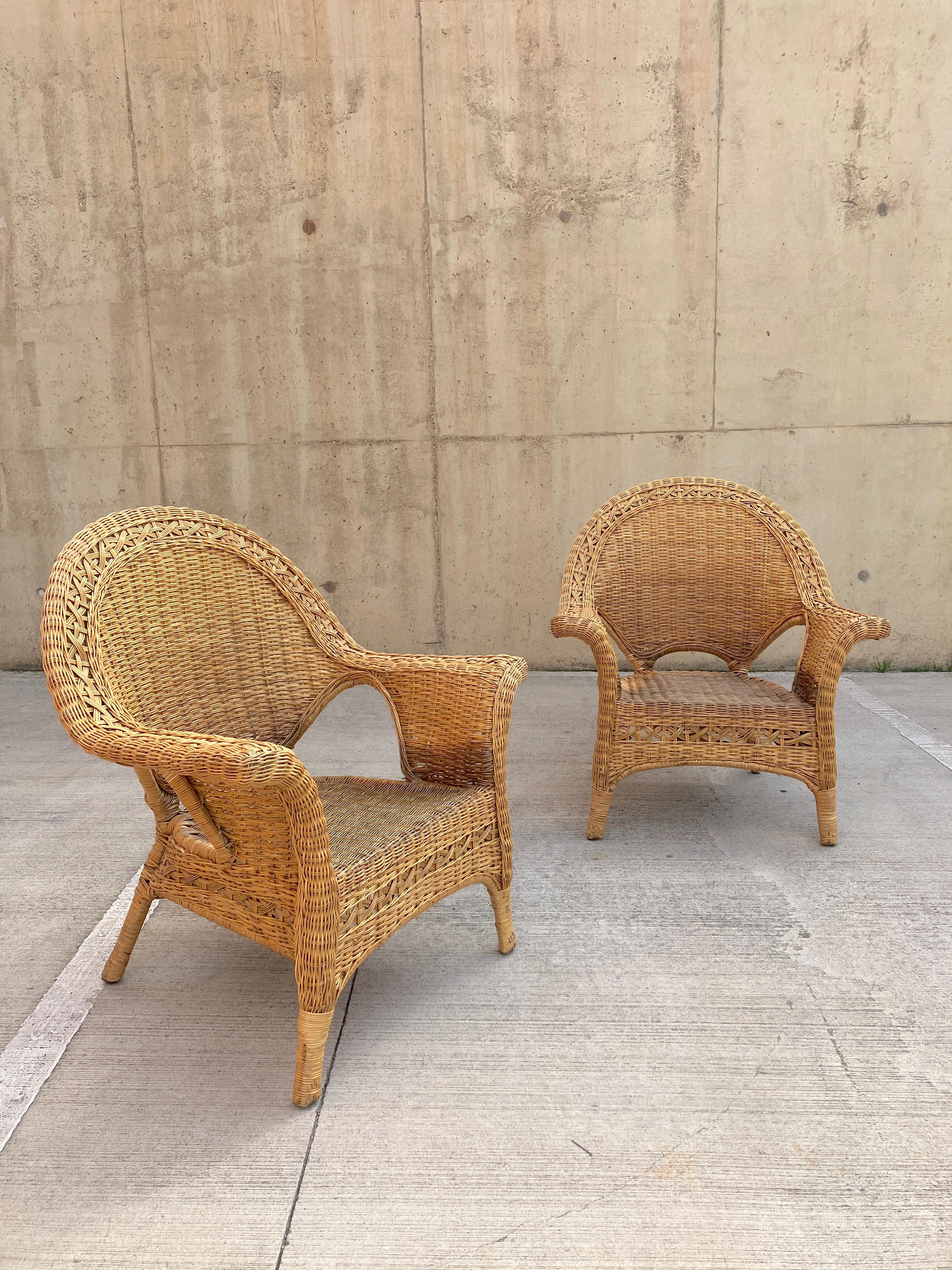 A sculptural pair of 20th-century wicker armchairs in rattan. The vintage chairs have gorgeous large open armrests beautifully woven. The wicker armchairs are made with an attractive cane base that has been expertly woven with rattan. 

Very large