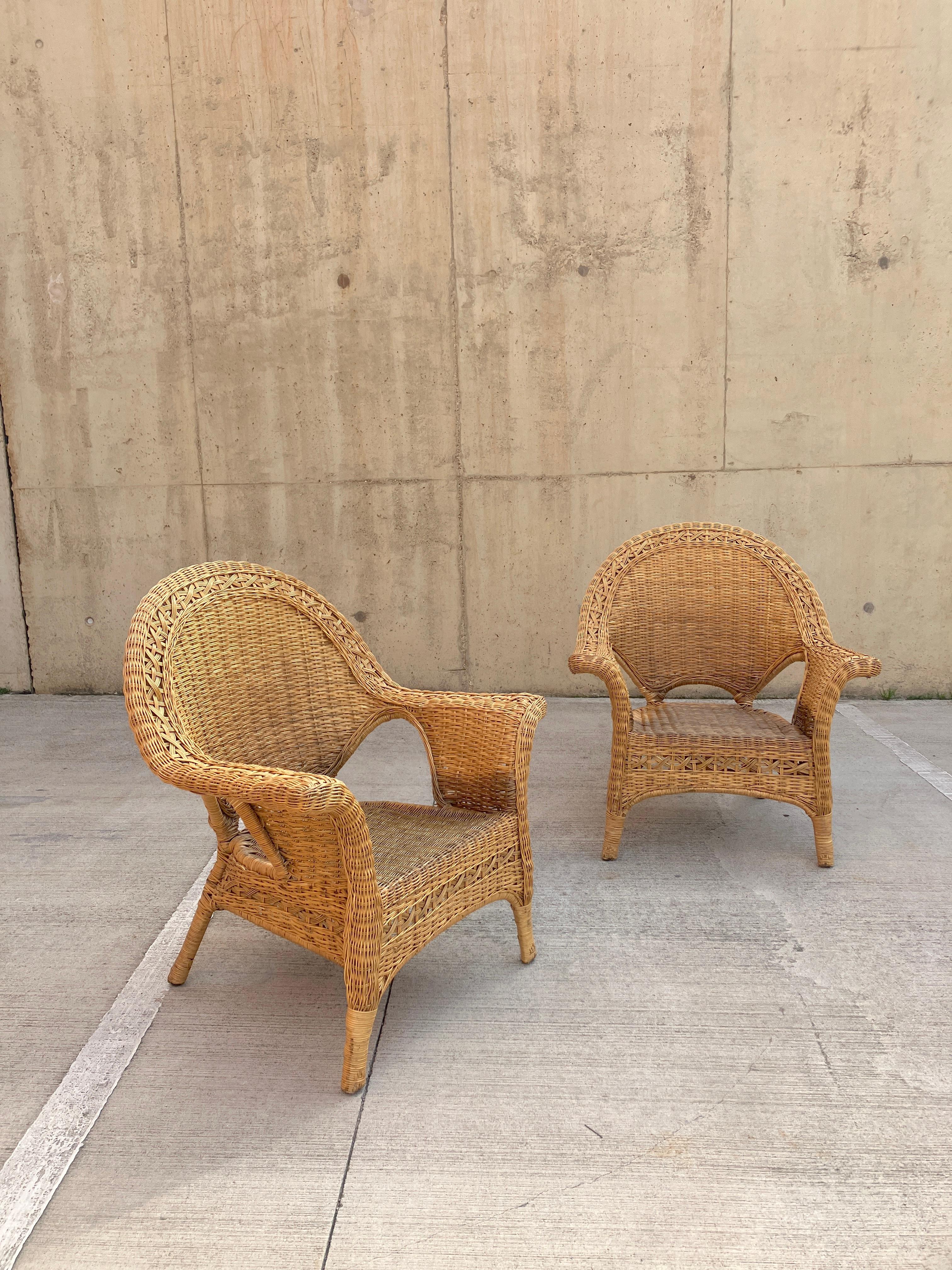 Una coppia scultorea di poltrone in vimini in rattan del XX secolo. Le sedie vintage hanno degli splendidi braccioli aperti di grandi dimensioni che sono intrecciati in modo meraviglioso. Le poltrone in vimini sono realizzate con un'attraente base
