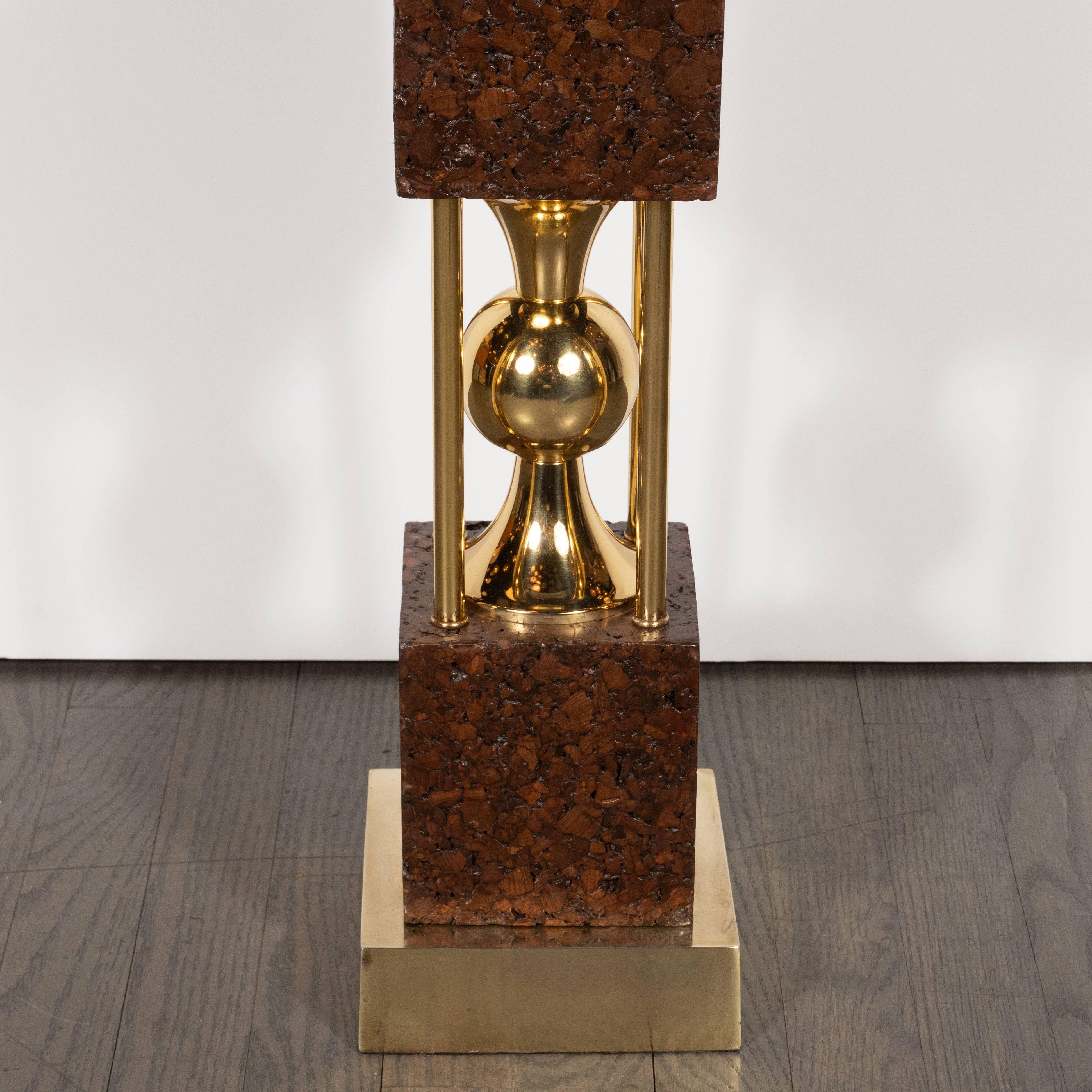 This stunning and graphic pair of table lamps were realized in the United States, circa 1960. They feature three square forms in cork finished in a burnt umber brown separated by hourglass forms that adjoin an orbital center in polished brass. Two