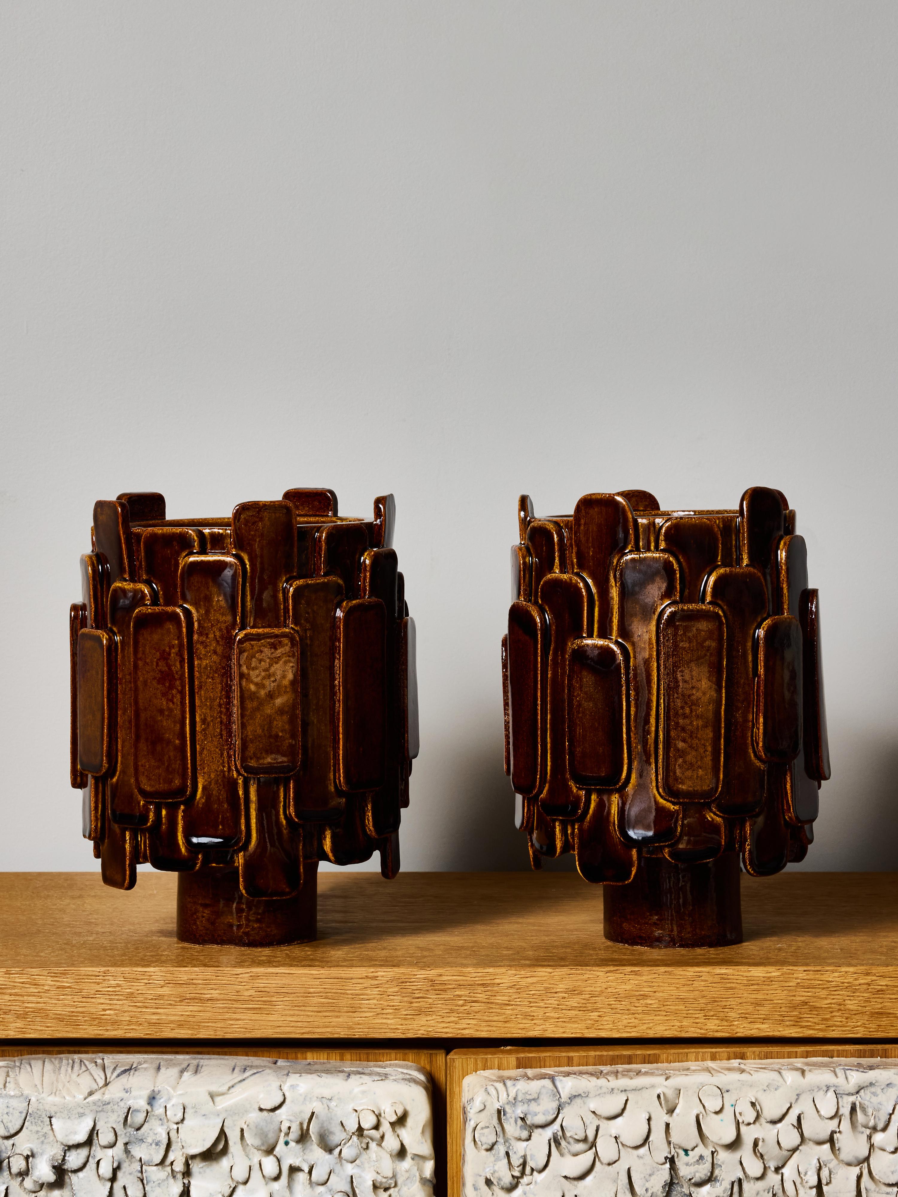 Este llamativo par de lámparas de mesa de cerámica de la artista francesa Adeline Delesalle muestra su característico enfoque escultórico de la forma y la superficie. Cada lámpara se construye con elementos cerámicos en capas, formados a mano y