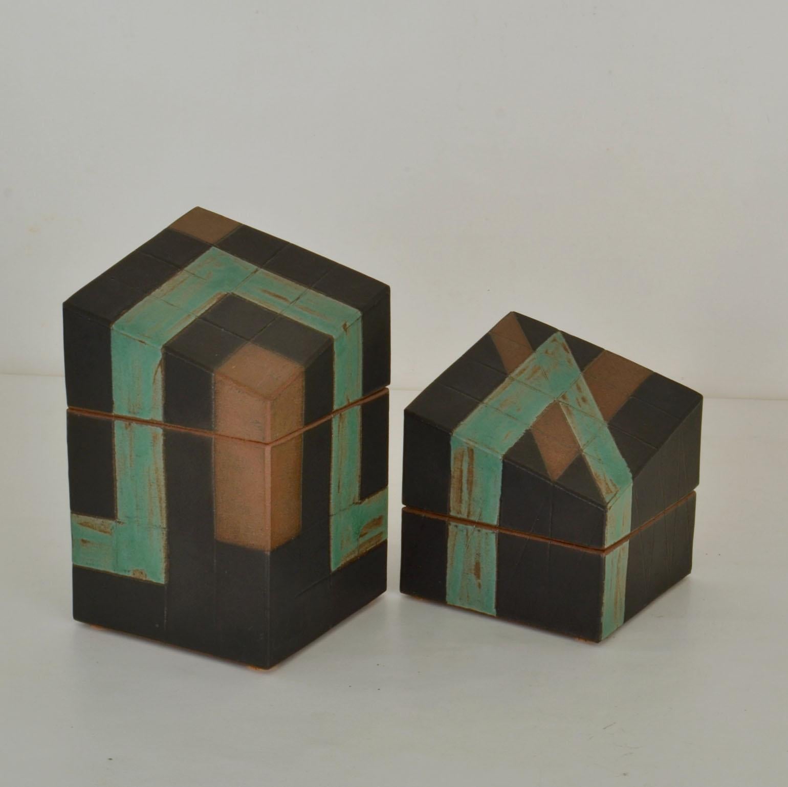 Sculptural square Studio Pottery boxes with slanting tops, signed PS. The geometric pattern in sage green and brown on the black boxes is designed to continue from one box to the other. The lids fit precisely on the bases of the late 20th century