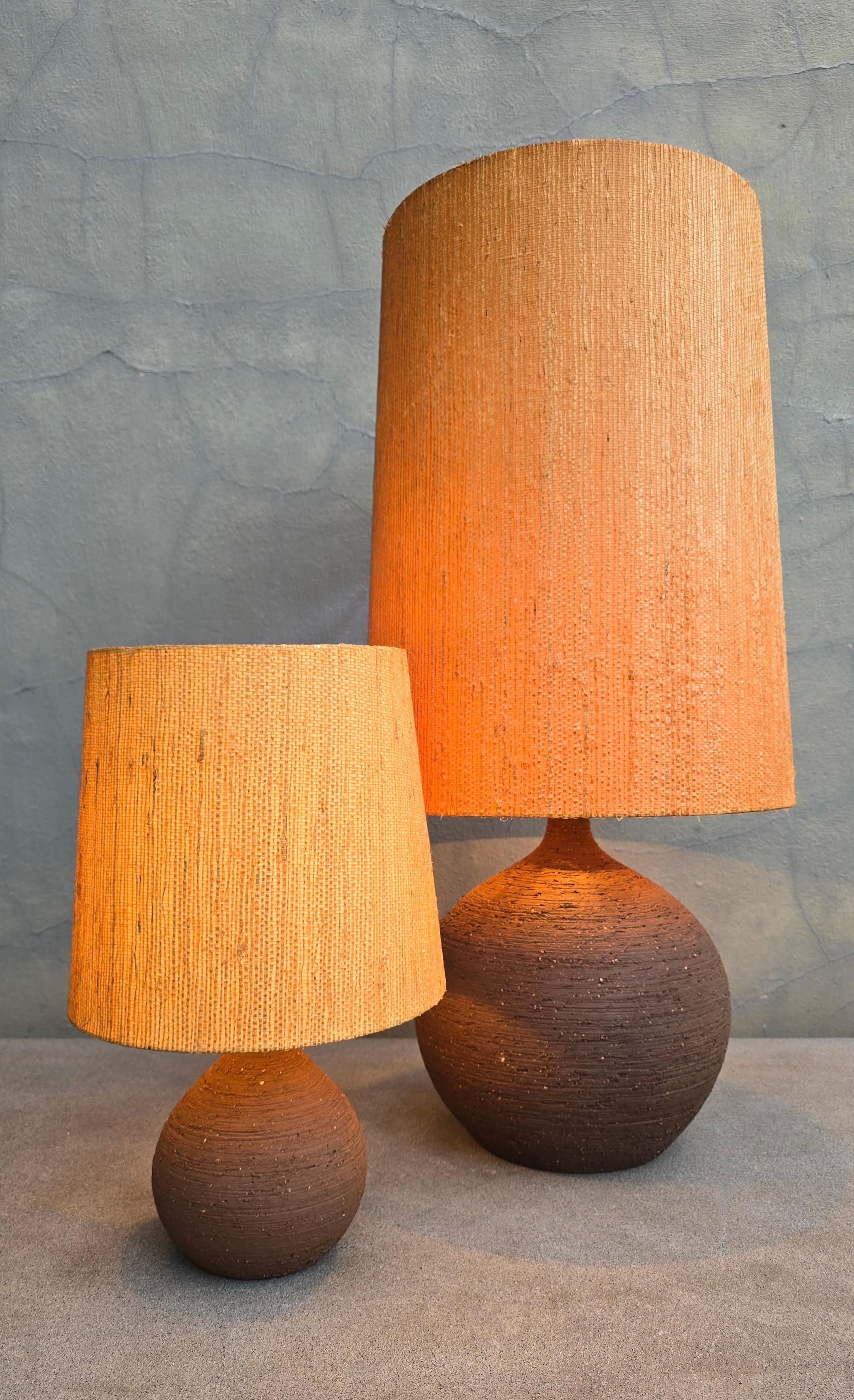 Paire unique de lampes de table en poterie de studio belge des années 1970, fabriquées à la main en céramique chamottée texturée et accompagnées de leur abat-jour original en paille tressée à la main. Des formes organiques sculpturales à la présence