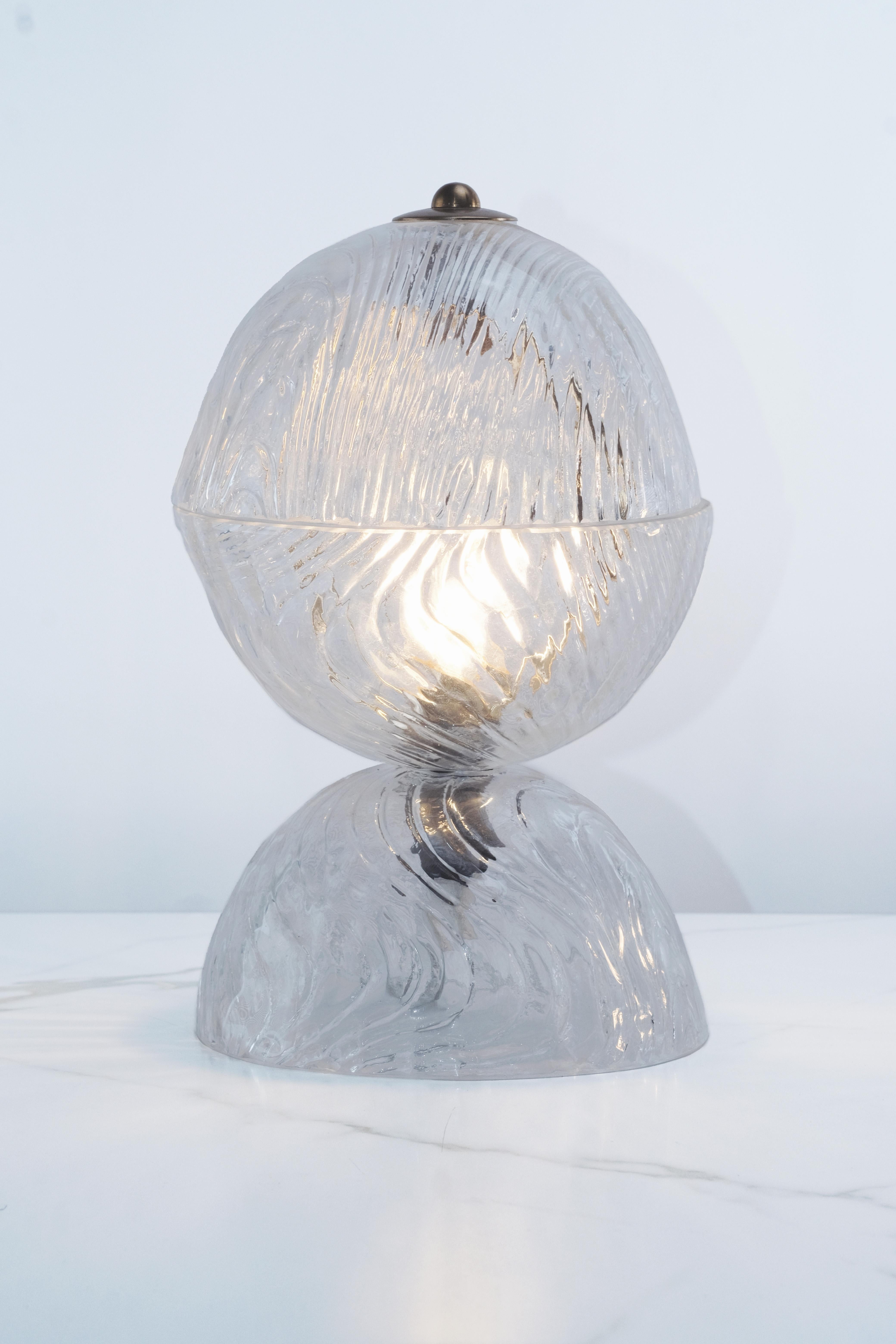 A stunning pair of Italian Murano glass table lamps from the 1970s, each composed of two handblown, swirled clear glass hemispheres stacked to create a harmonious sculptural silhouette. The dynamic swirling texture of the glass catches and refracts