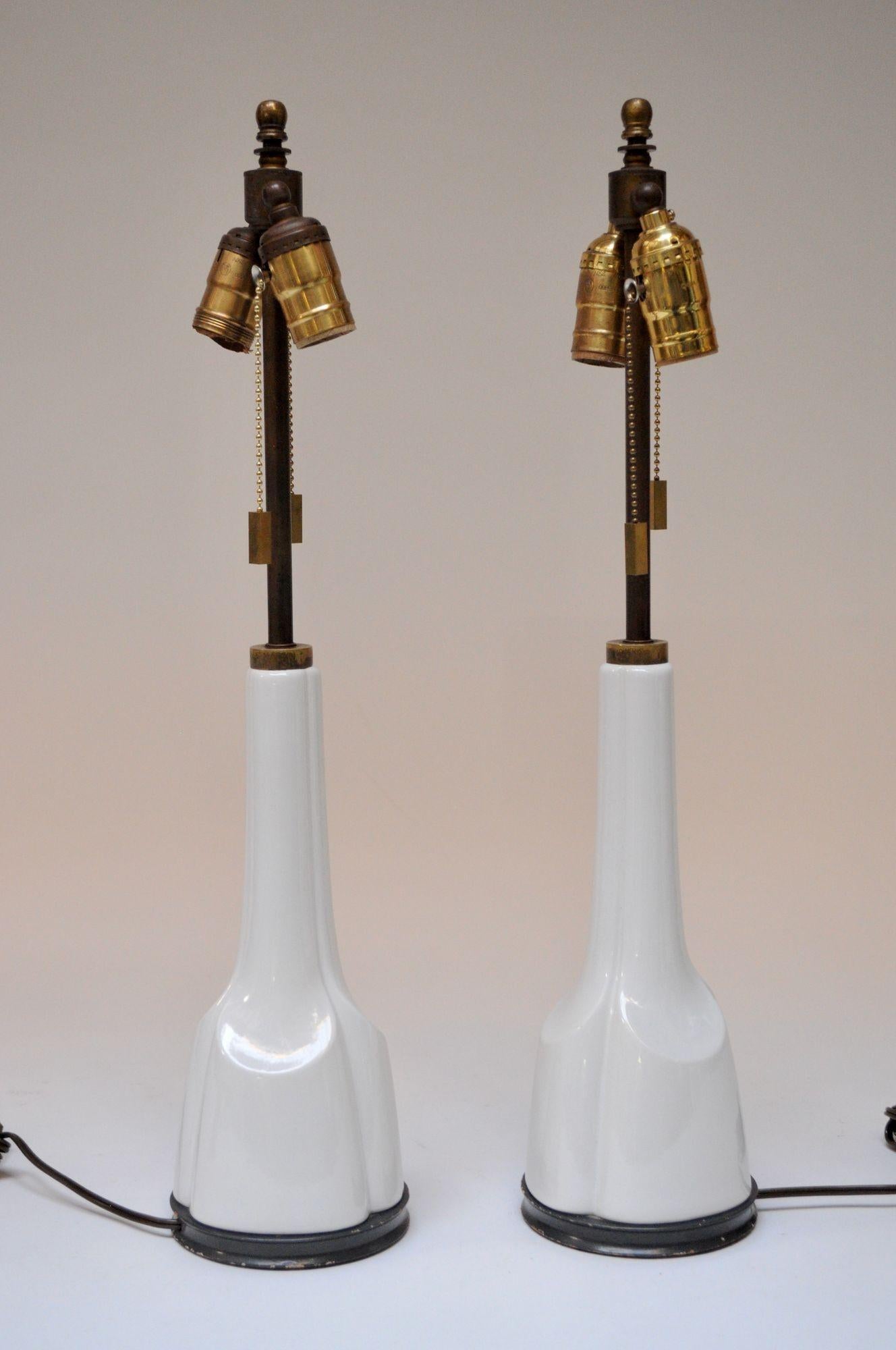 Pair of Mid-Century American Modern tables lamps (ca. 1950s, USA). Composed of patinated brass stems and white porcelain forms, all supported by ebonized wooden platform bases. Along with the wiring, the dual brass sockets and on/off pull strings