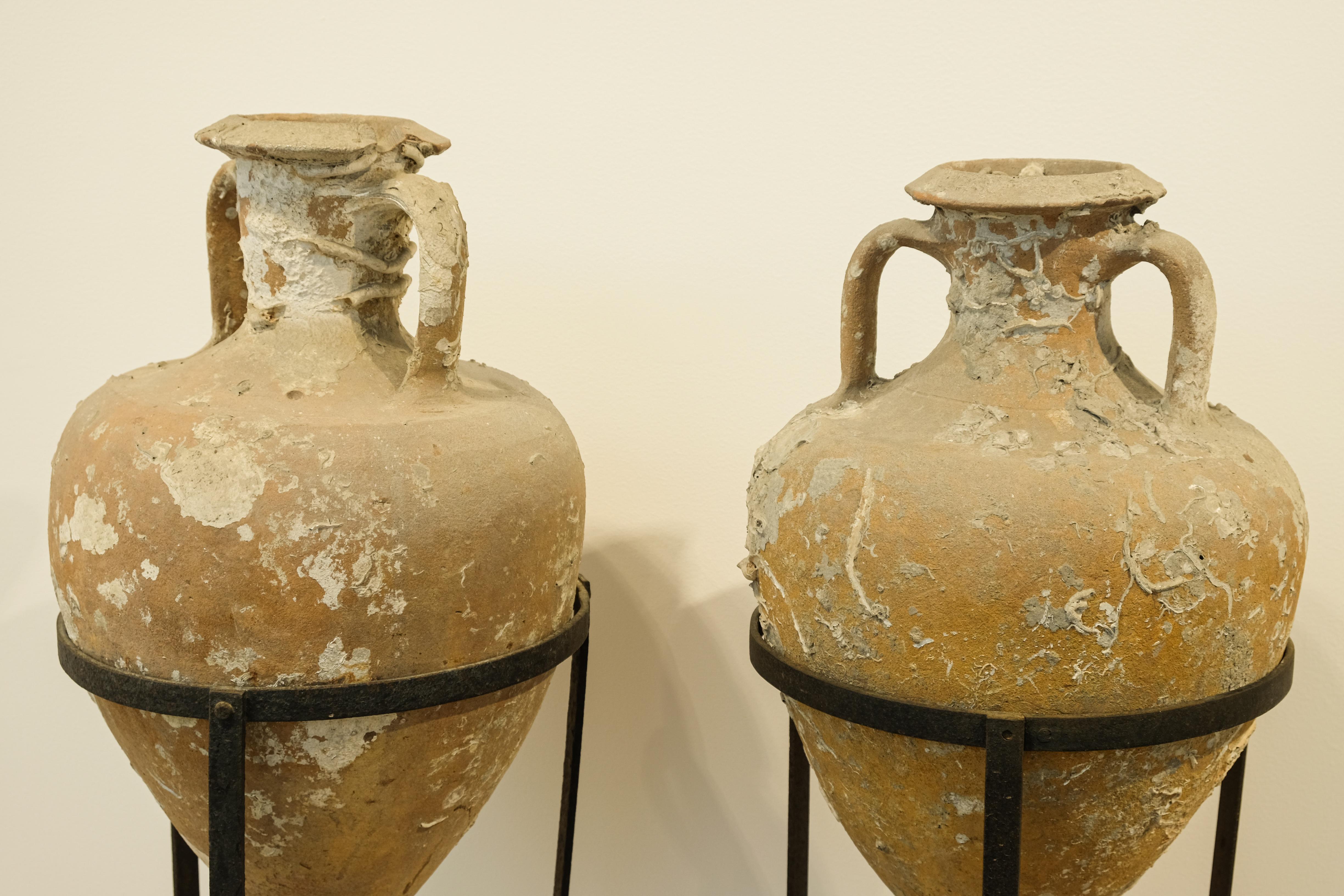 A pair of Roman sea salvaged amphorae likely 2nd-3rd century, with 19th century wrought iron stands. Amphorae were designed for marine transport of wine and found in shipwrecks dating back to the bronze age. Beautiful sea encrustations and patina.