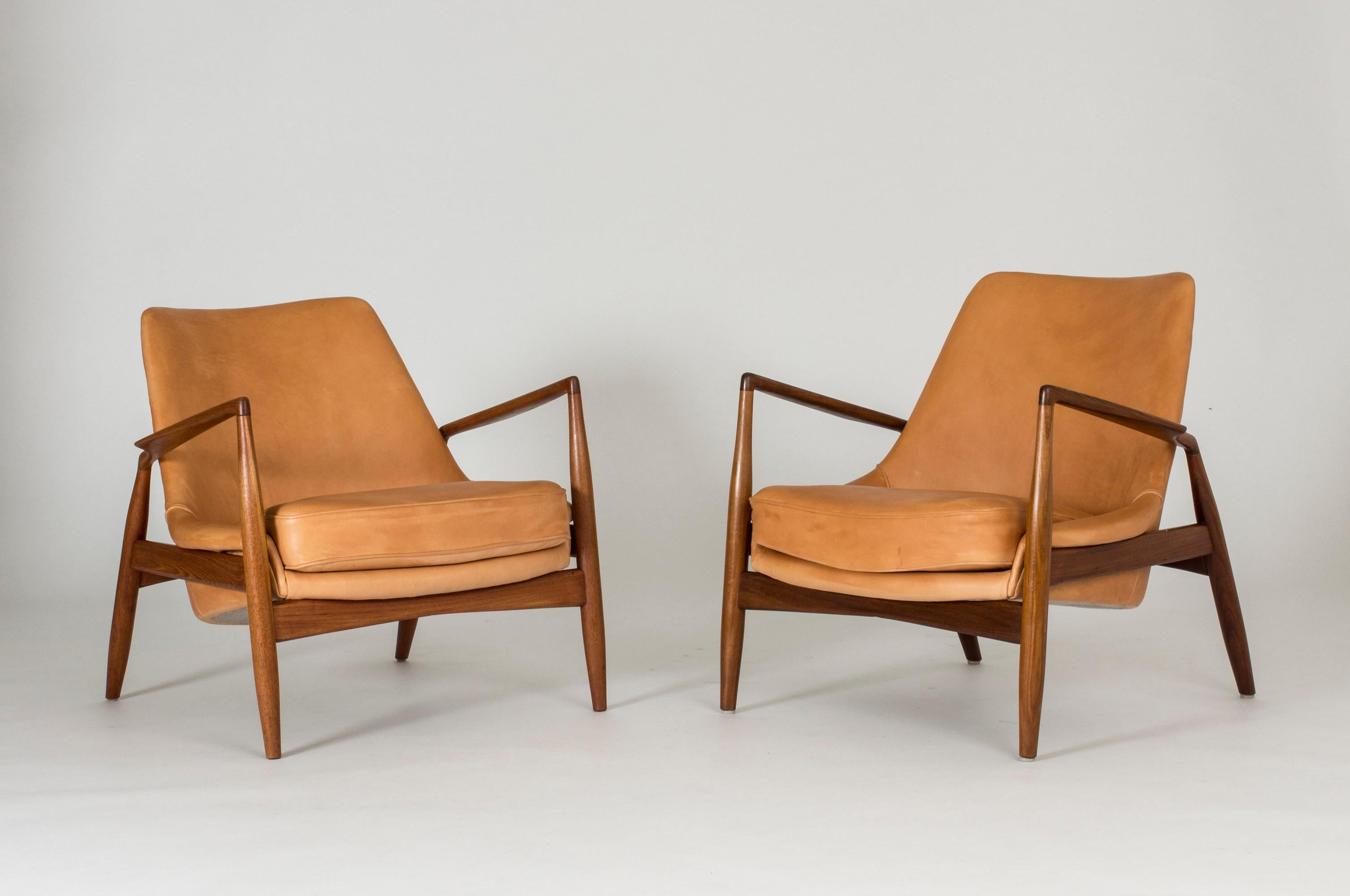 Pair of amazing “Seal” lounge chairs by Ib Kofod Larsen, made with teak frames and beautiful, smooth cognac colored leather. Great silhouettes and materials, sculpted winglike armrests.