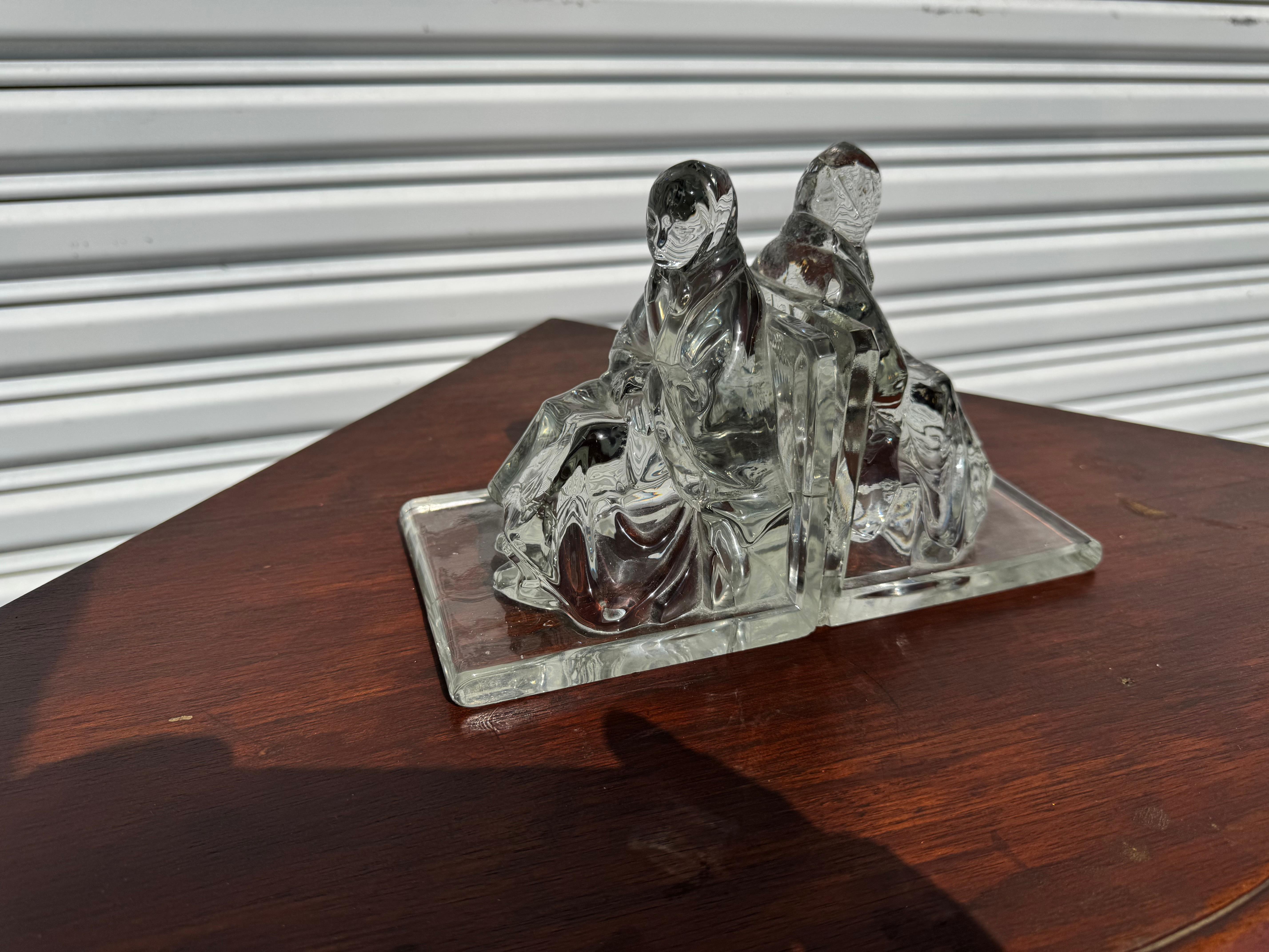 This pair of bookends are made of molded glass.
They depict 2 women seated.
