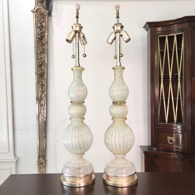 Pair of original grand scale Murano glass table lamps by Archimede Seguso imported by The Marbro Lamp Co. circa 1960. Both lamps signed. 
Ribbed opalescent silvery white glass with flecks of gold. Bases have been platinum leafed with a gold wash.