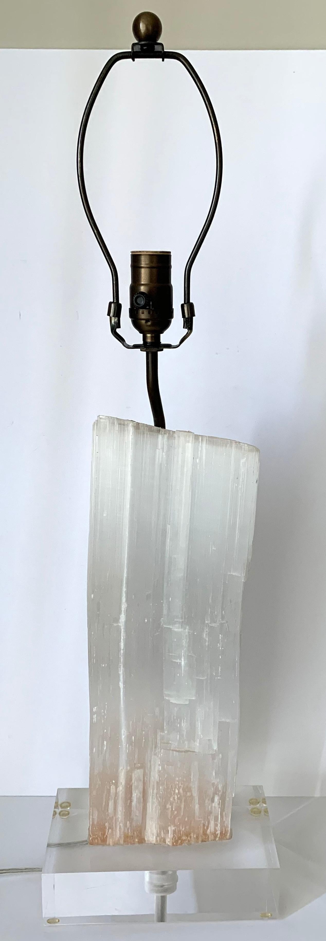 Pair of selenite lamps on thick clear Lucite bases. Selenite has naturally occurring variances in color and has a very subtle pink hue in certain light. Adjustable single sockets extend up to 24