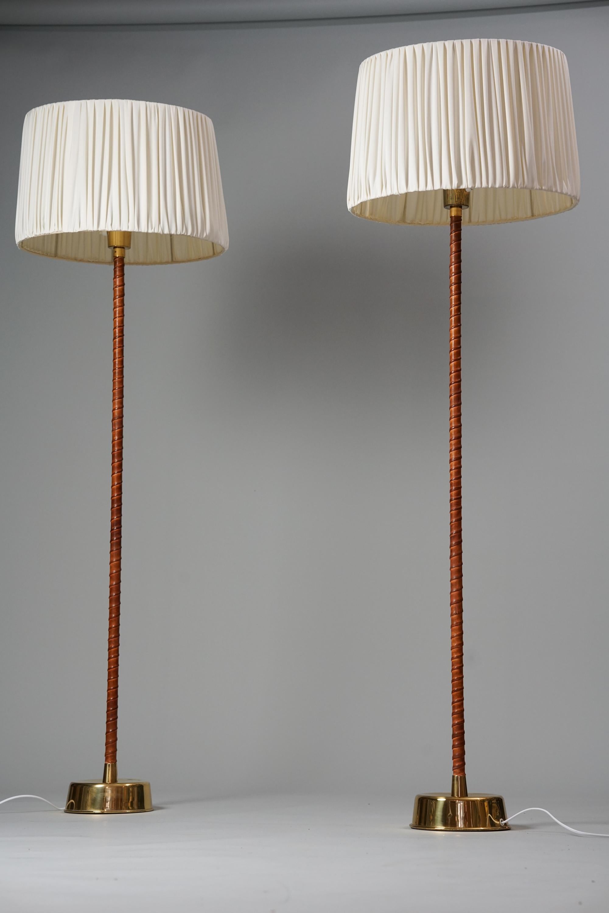 Pair of Senator floor lamps, design Lisa Johansson-Pape, manufactured by Orno Oy, 1950s. Leather and brass with cotton lampshades. Good vintage condition, minor patina consistent with age and use. The floor lamps are sold as a set. 

Lisa