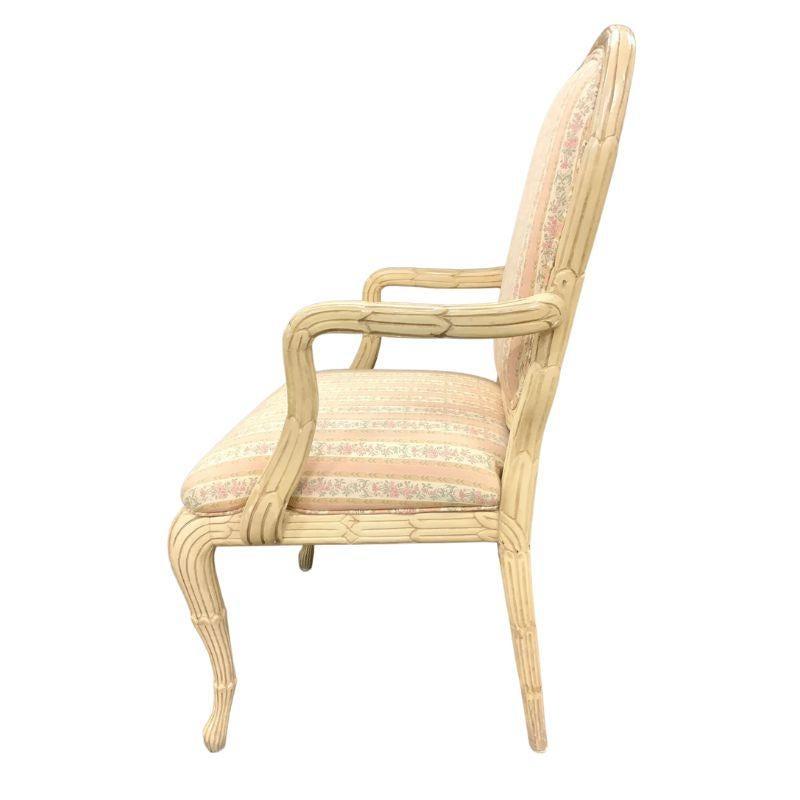 A pair of Serge Roche style arm chairs with pink floral striped fabric.  The carved and painted cream color chairs with rounded back and curved arms and legs have a distinctive palm frond design to the frame.  The upholstery is a floral and vine