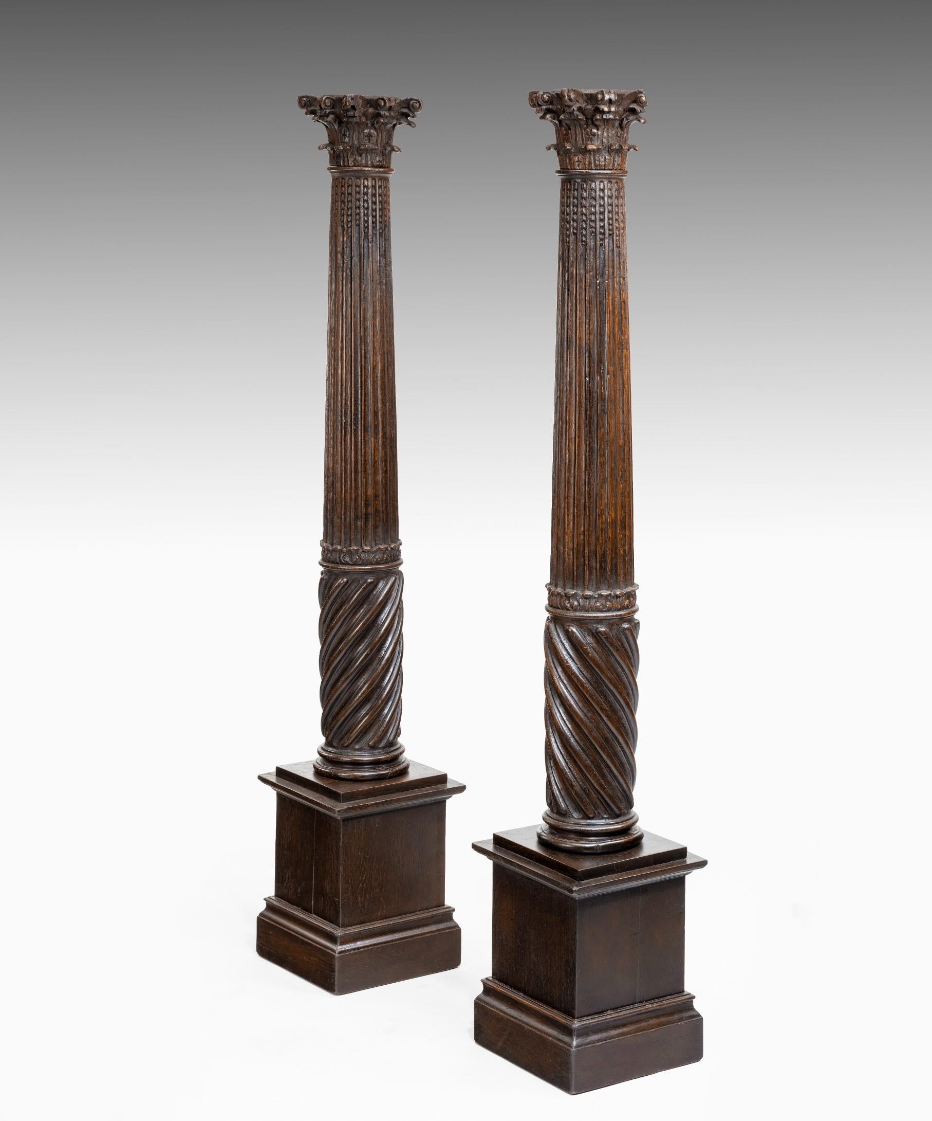 A wonderfully atmospheric pair of 17th century carved oak columns; the composite capital raised on a fluted and spiral turned column which terminates in a modern pedestal base.