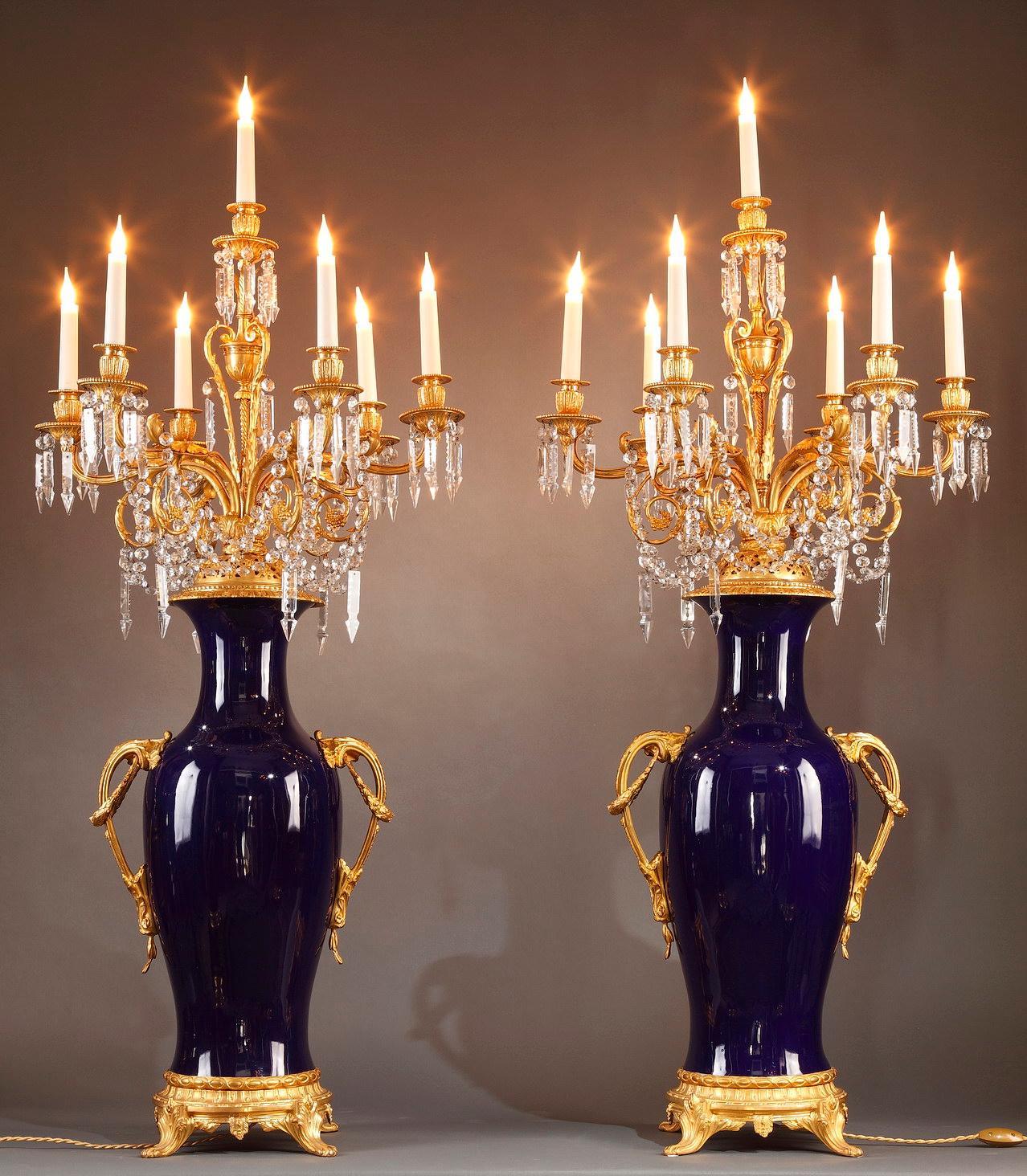 Large pair of baluster-shaped candelabra vases with seven lights, in gros bleu porcelain and chiselled and gilded bronze. The sconces, adorned with foliage and vine branches, are joined by elegant garlands of crystals cut in prisms and mirzas. Two