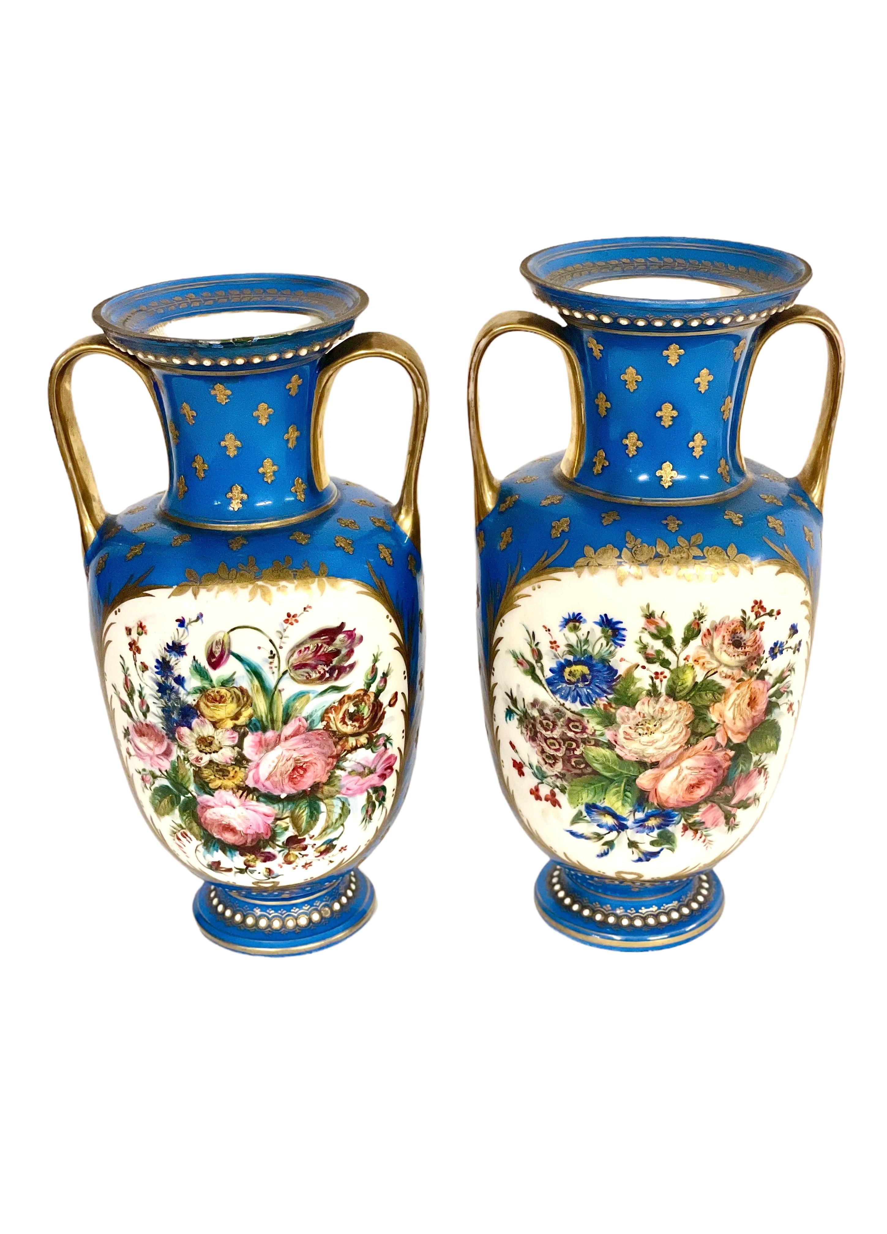 A beautiful pair of hand-painted Charles X Sèvres porcelain vases, painted in classical blue, with fleur-de-lis on the neck, gilded handles and pearl decoration. The front scenes depict frolicking cupids on a background of flowers within a gilded