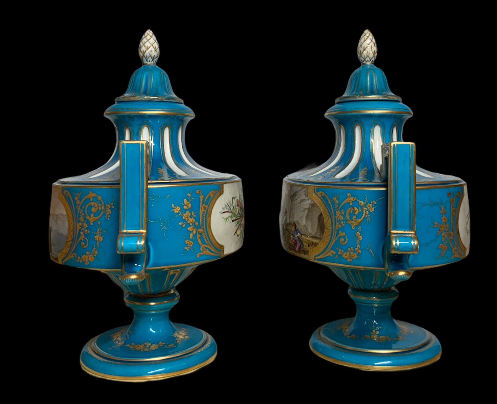 This is a pair of Sevres hand painted porcelain turquoise lidded urns. Both of them are depicting in the front a sea shore fishermen scenes. In one, a group of fishermen are preparing a sailboat and in the other one, they are pulling the net. The