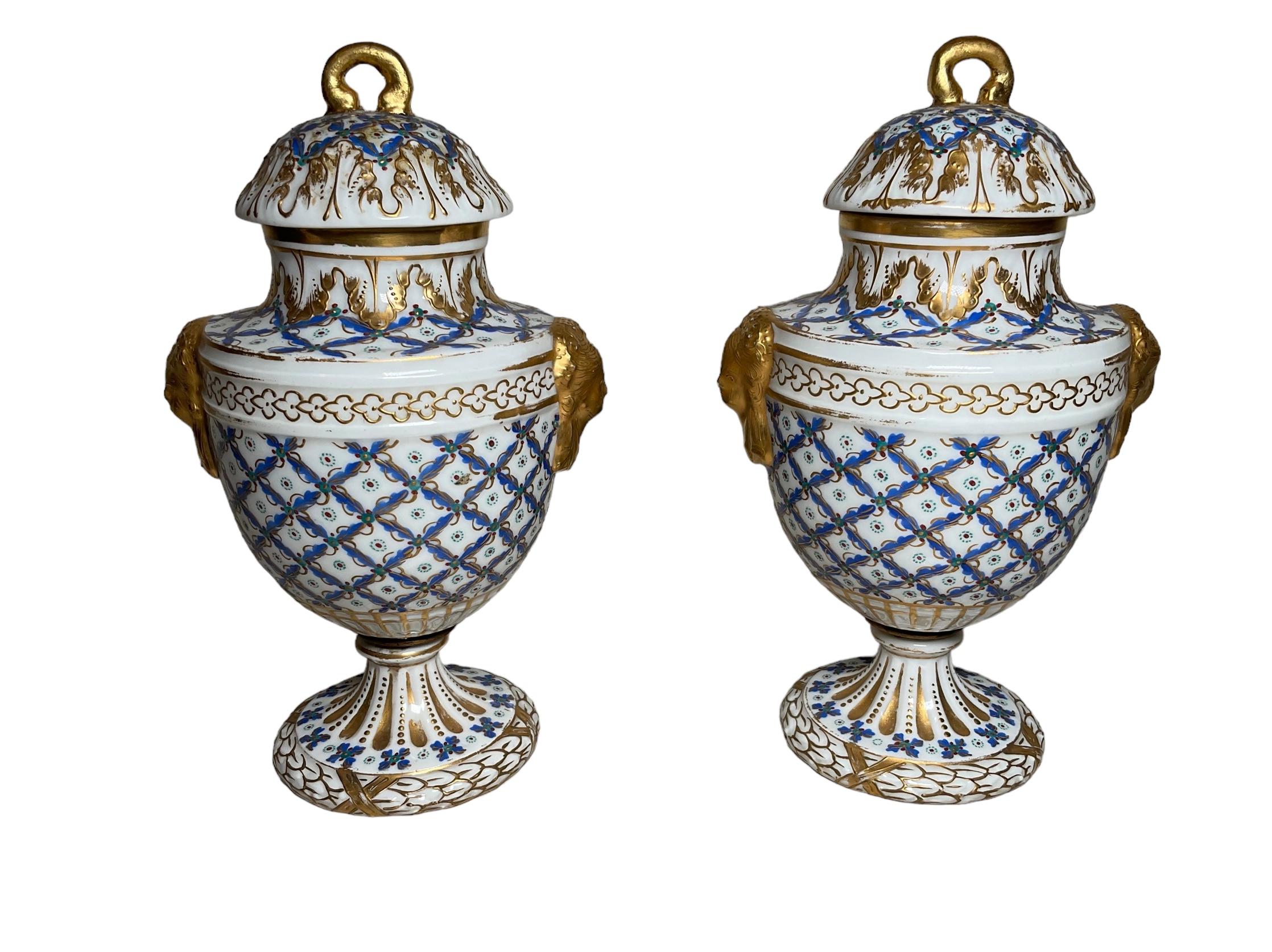 This is a pair of hand painted Sevres porcelain lidded small urns. It depicts a medium Size urns hand painted with a gilt lattice pattern where the blue, white and green colors predominate together with the gold. Some gilt white acanthus leaves