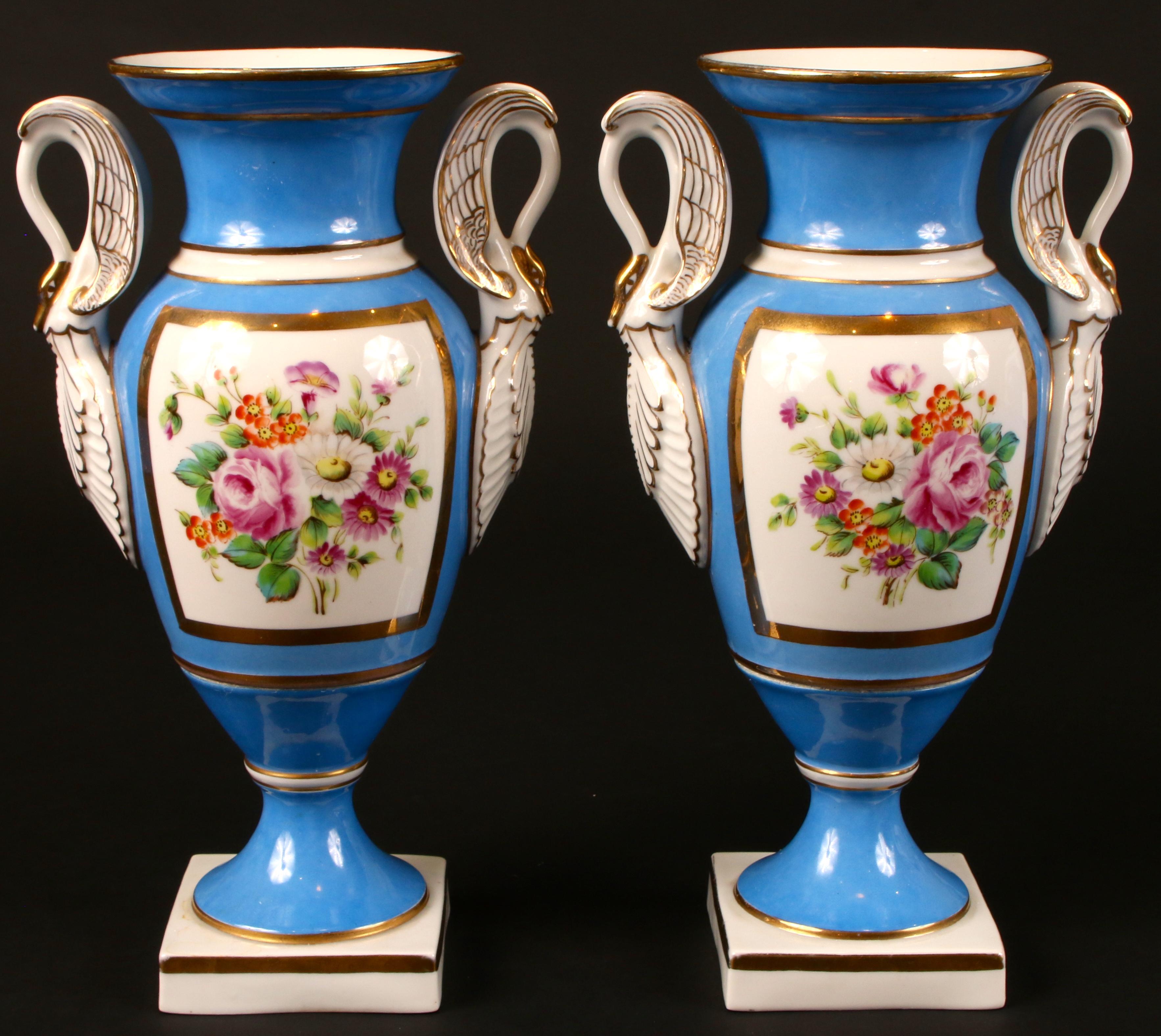Gorgeous vintage pair of blue and gold Serves style porcelain urn vases. Beautiful deep blue background with hand painted floral bouquets on one side and a gold star on the other. Side handles are white and gold swans. Mounted on square