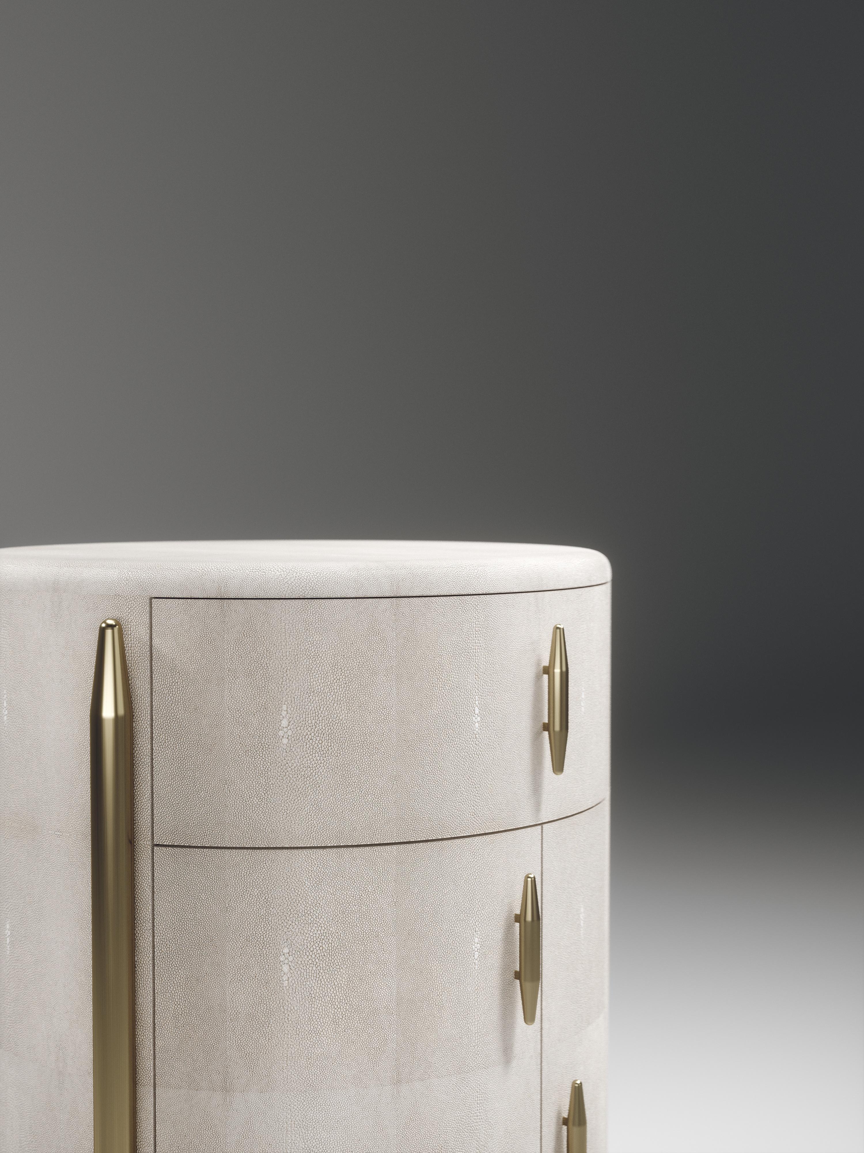The Pair of dandy round bedside tables by Kifu Paris are elegant and luxurious home accents, inlaid in cream shagreen with bronze-patina brass details. This piece includes 1 drawer total and a cabinet below; the interiors are inlaid in gemelina wood