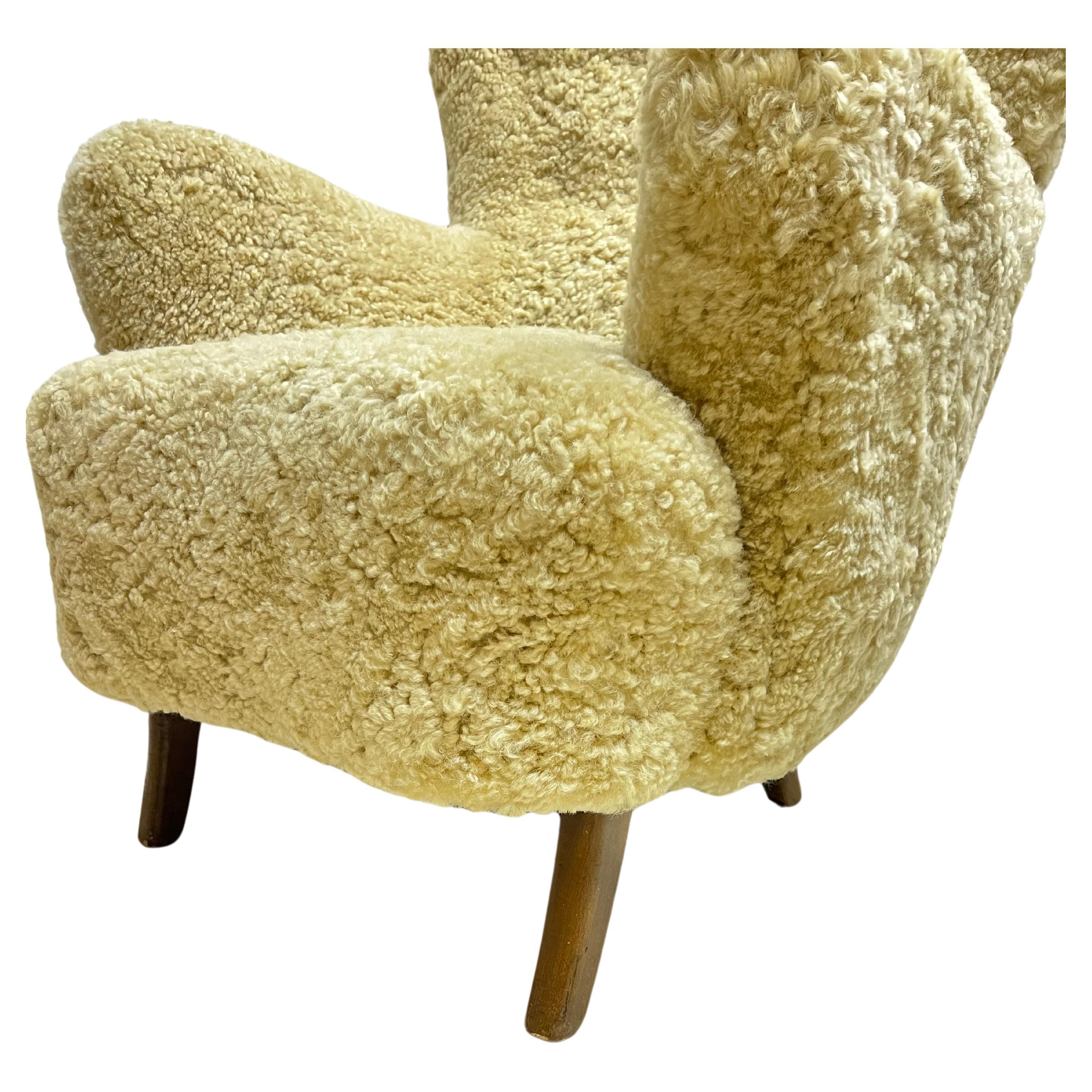 A pair of Danish Modern high-backed lounge chairs by Danish designer, Alfred Christensen, newly recovered in natural honey colored sheepskin, with curved arms. Circa 1950s.

About the Designer: In 1936, Christensen joined Knoll as a designer and