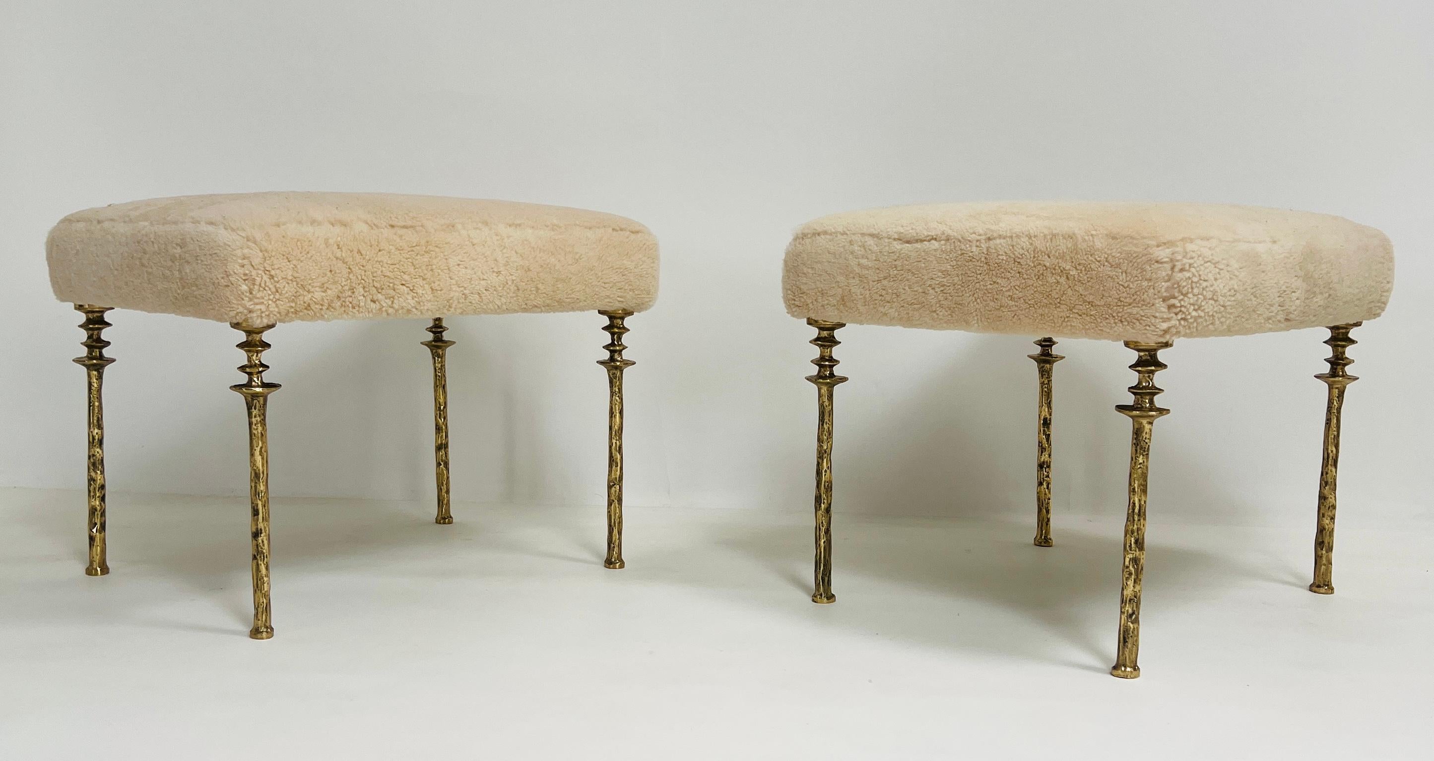 Due sgabelli Sorgue, una lussuosa fusione di raffinatezza e comfort. Questo modello presenta gambe in bronzo dorato, squisitamente fuse per incarnare un'eleganza senza tempo, e un cuscino in shearling naturale che offre una seduta morbida e