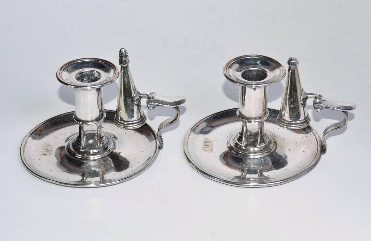 The pair of Sheffield silver plate chamber sticks have attached snuffers. The handles fit the first and second fingers and have thumb rests. The base metal is copper. The one candleholder is stamped James Dixon & Sons, while the other has a missing