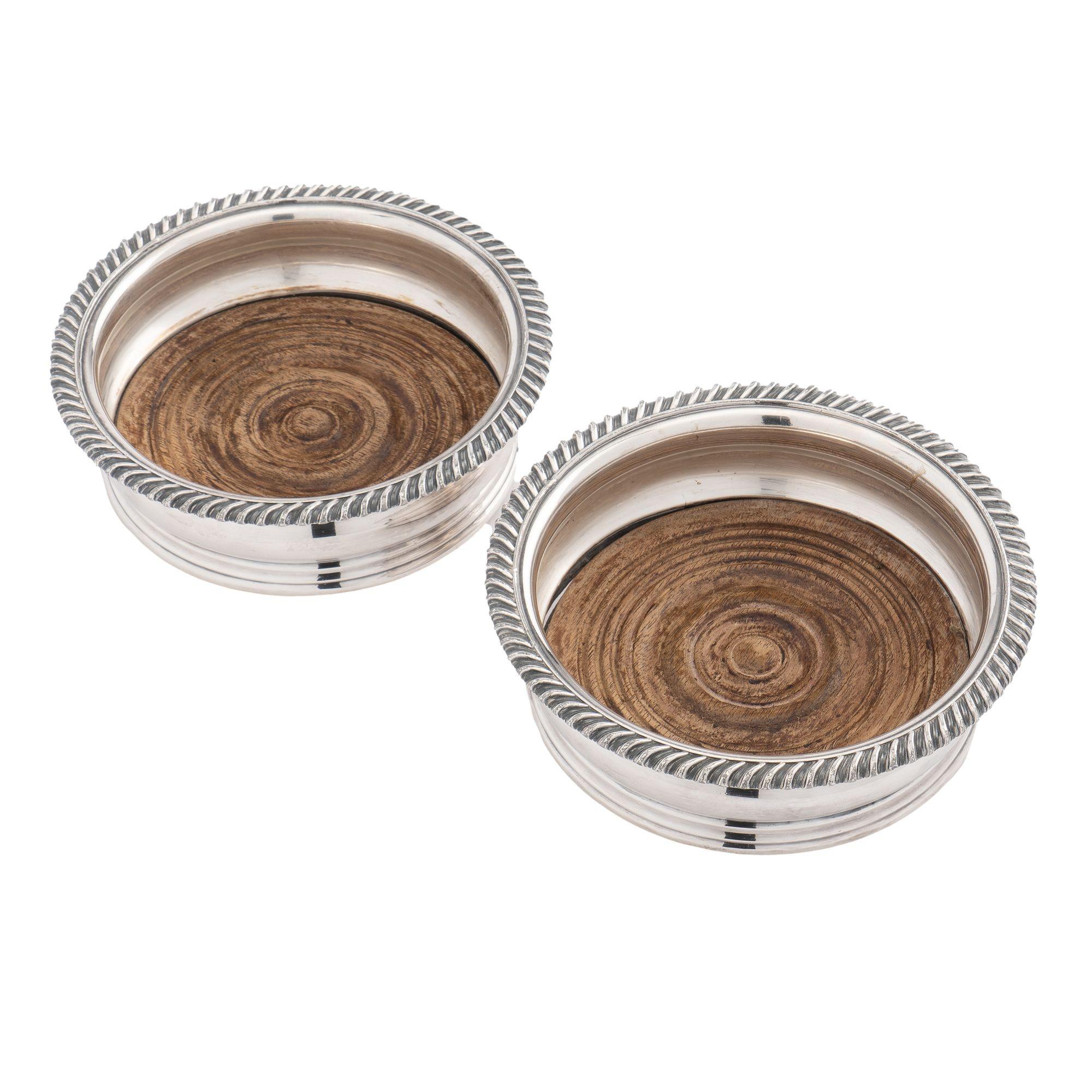 Pair of Sheffield silver wine coasters with cast gadroon edges on Bombay sides. Fitted with a turned wood base on a green baize footing.
England, circa 1830.