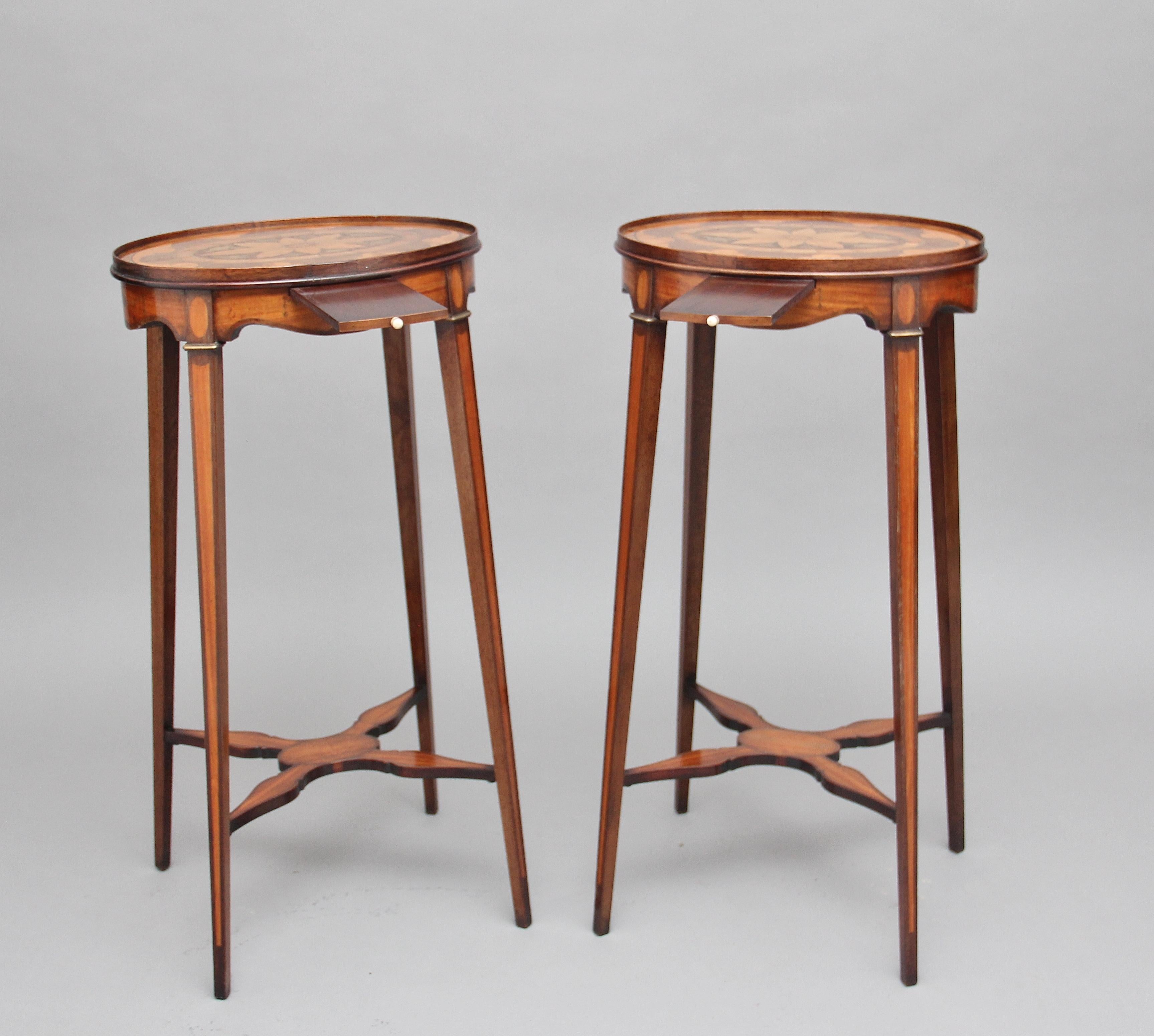 A pair of Sheraton revival mahogany and inlaid oval urn stands, the oval tops profusely inlaid with a decorative pattern and floral decoration at the centre, having pull out candle slides and an inlaid shaped apron, supported on elegant square legs