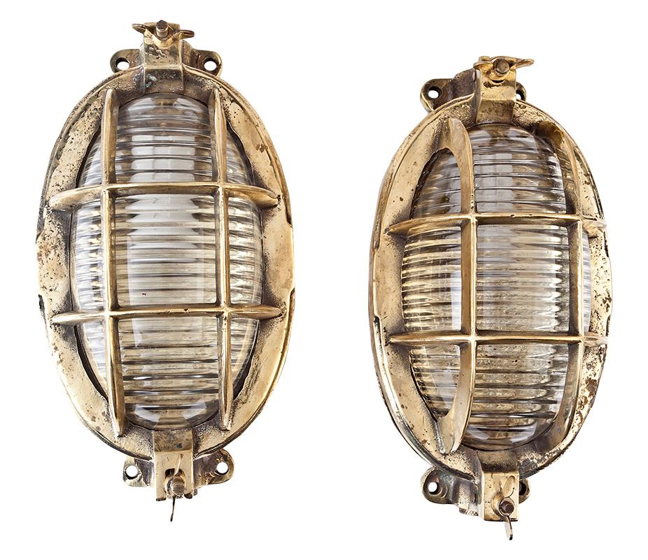 Pair of original ship's brass passageway lights with Fresnel lens glass shades. The overlying brass cage is hinged on one end and a dog latch on the opposite end gains access to the bulb. The socket takes a standard base light bulb. Rewired for